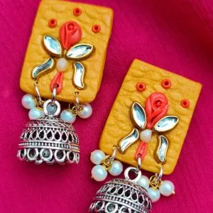 These vibrant yellow jhumka earrings are a fun mix of tradition and modern style. The square-shaped top has a textured surface, decorated with a colorful rosette motif. The earrings are finished with silver oxidized jhumkas and tiny pearl drops, adding a delicate touch.