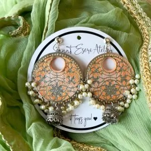 These big round peach earrings are perfect for any occasion! They have a beautiful handmade design with small pearls and antique silver jhumkas hanging at the bottom. The unique pattern gives them a stylish and traditional look, making them great for weddings, festivals, and parties.