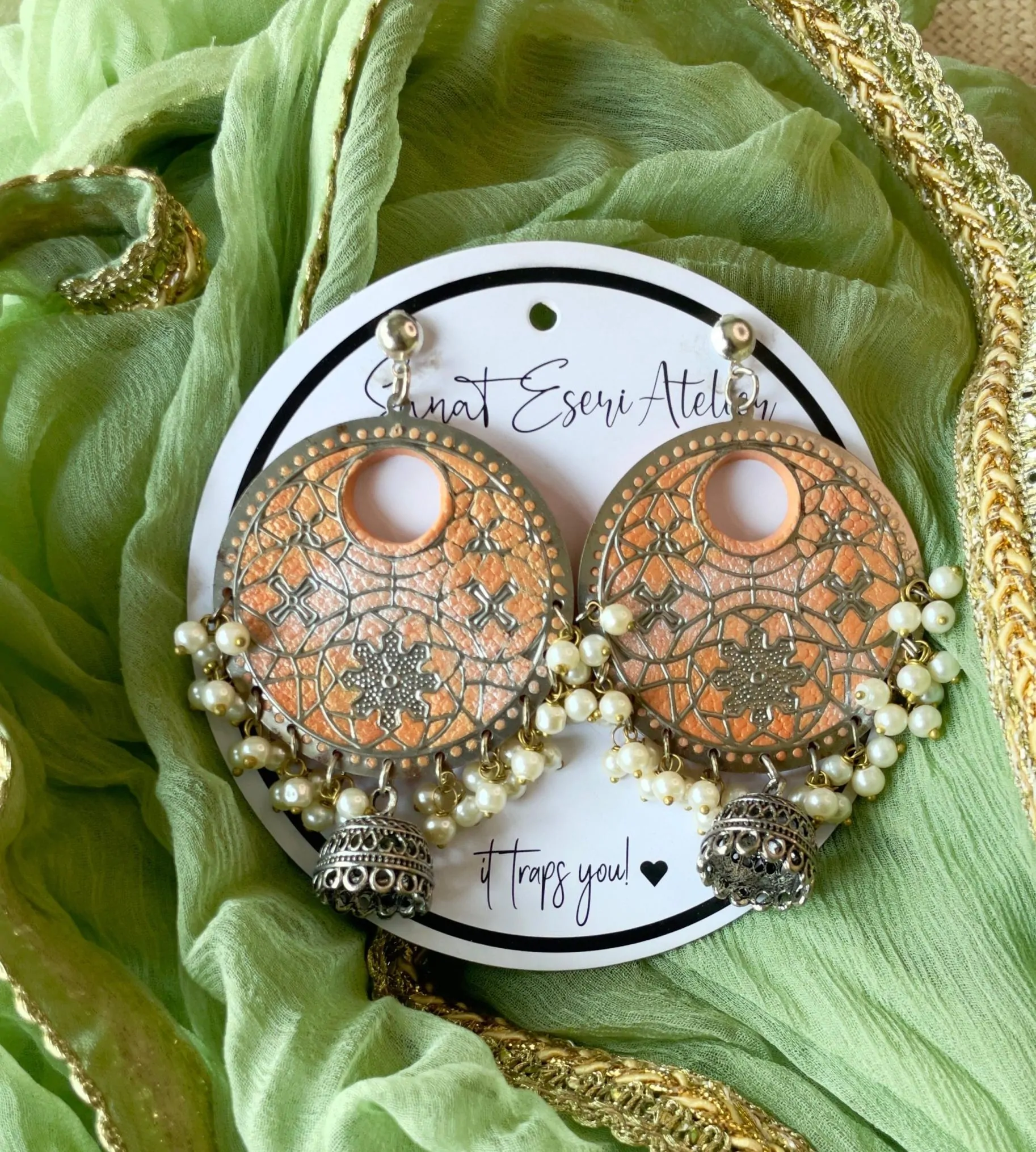 These big round peach earrings are perfect for any occasion! They have a beautiful handmade design with small pearls and antique silver jhumkas hanging at the bottom. The unique pattern gives them a stylish and traditional look, making them great for weddings, festivals, and parties.