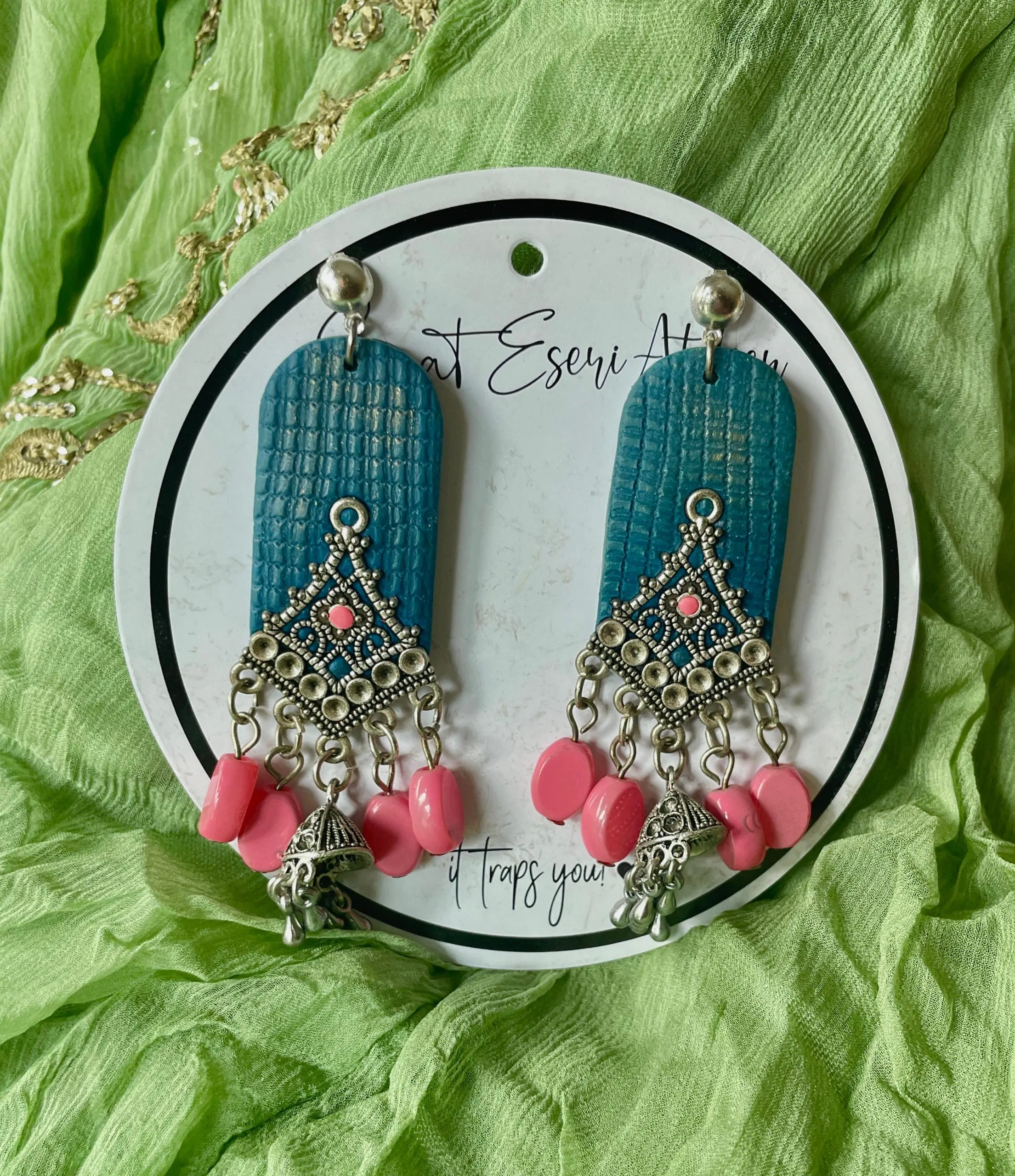 The highlight of this design is the intricate antique silver charm, shaped like a diamond with fine detailing and a central pearl. Below the charm, dangling pearl-like beads add a touch of grace and movement, along with small jhumka-style metallic bells.