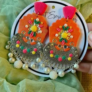 A vibrant and intricate blend of traditional and contemporary design elements, our antique silver crescent-shaped earring features a textured orange base with a floral embellishment made of colorful beads and sequins in pink, yellow, green, and white.