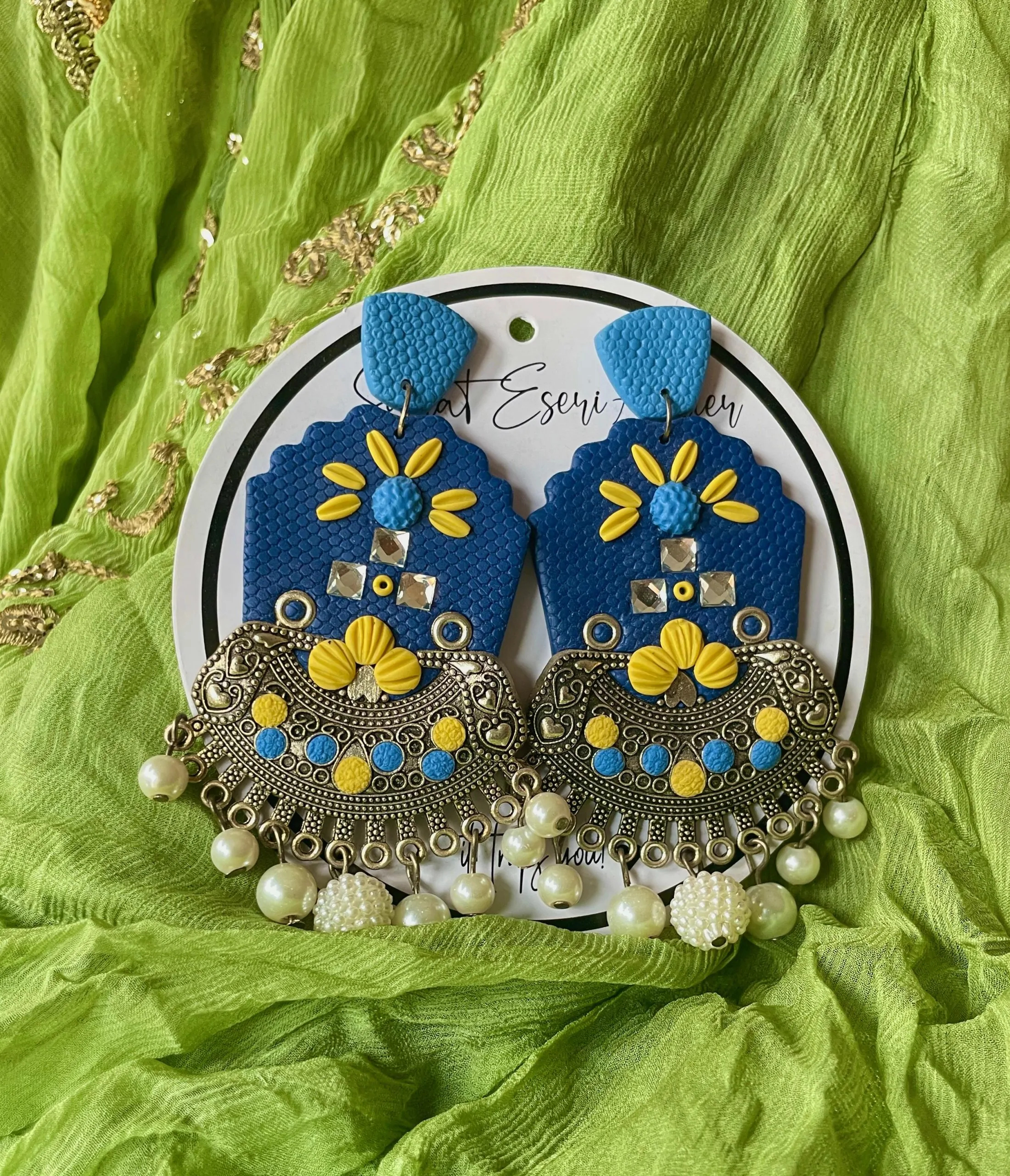 A vibrant and intricate blend of traditional and contemporary design elements, our antique silver crescent-shaped earring features a textured orange base with a floral embellishment made of colorful beads and sequins in pink, yellow, green, and white.