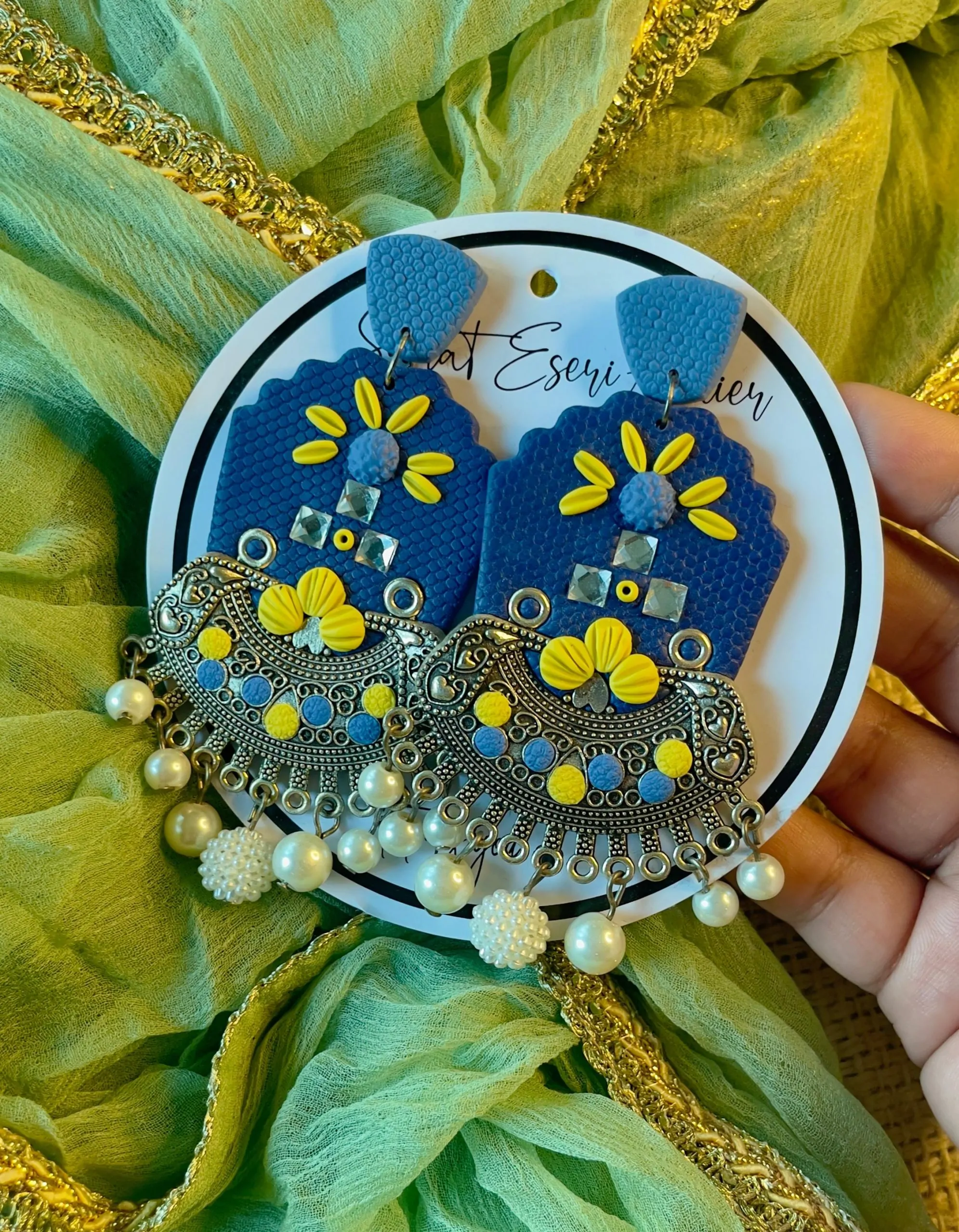 A vibrant and intricate blend of traditional and contemporary design elements, our antique silver crescent-shaped earring features a textured orange base with a floral embellishment made of colorful beads and sequins in pink, yellow, green, and white.