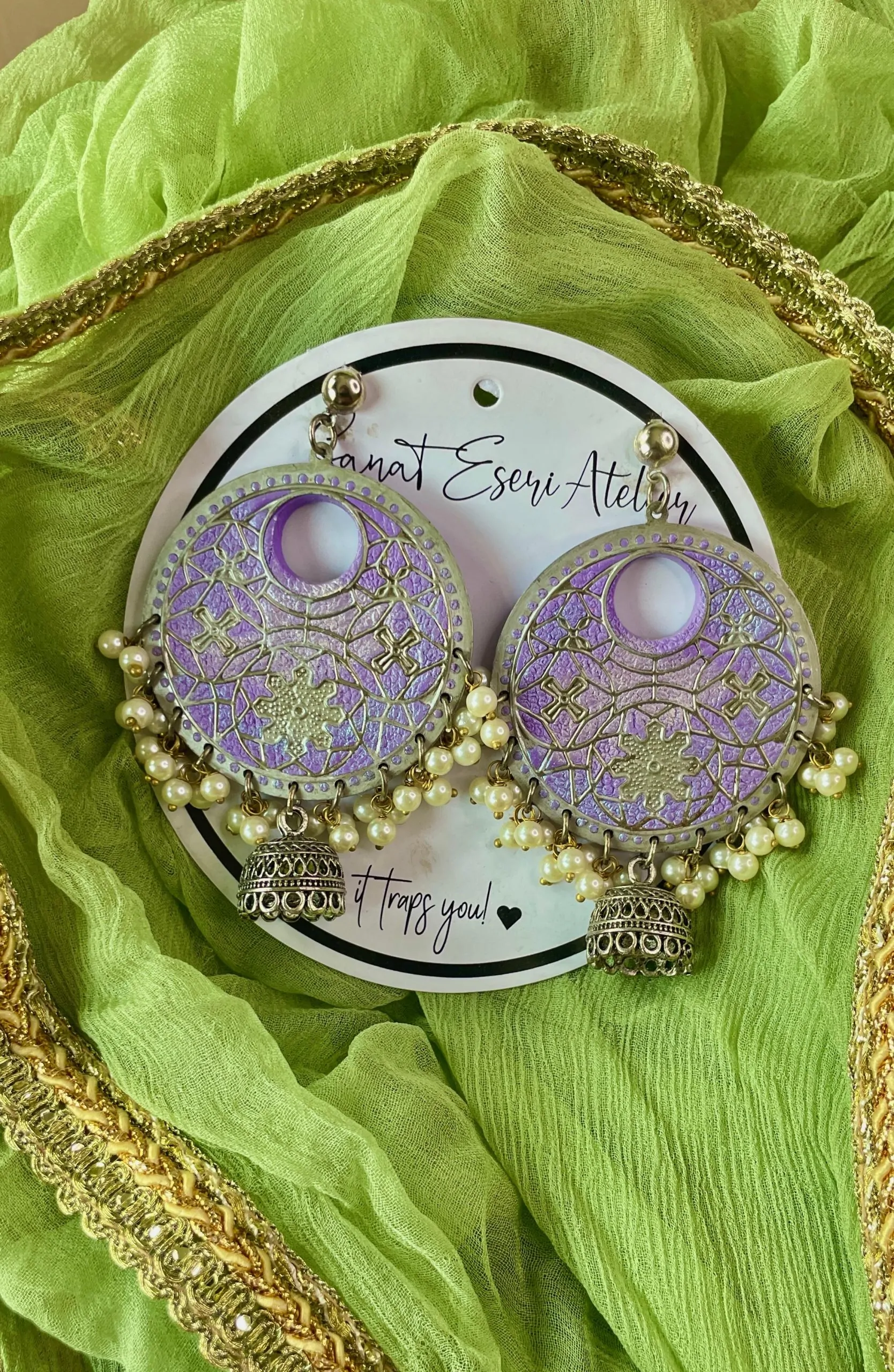 These big round lavender earrings are perfect for any occasion! They have a beautiful handmade design with small pearls and antique silver jhumkas hanging at the bottom. The unique pattern gives them a stylish and traditional look, making them great for weddings, festivals, and parties.