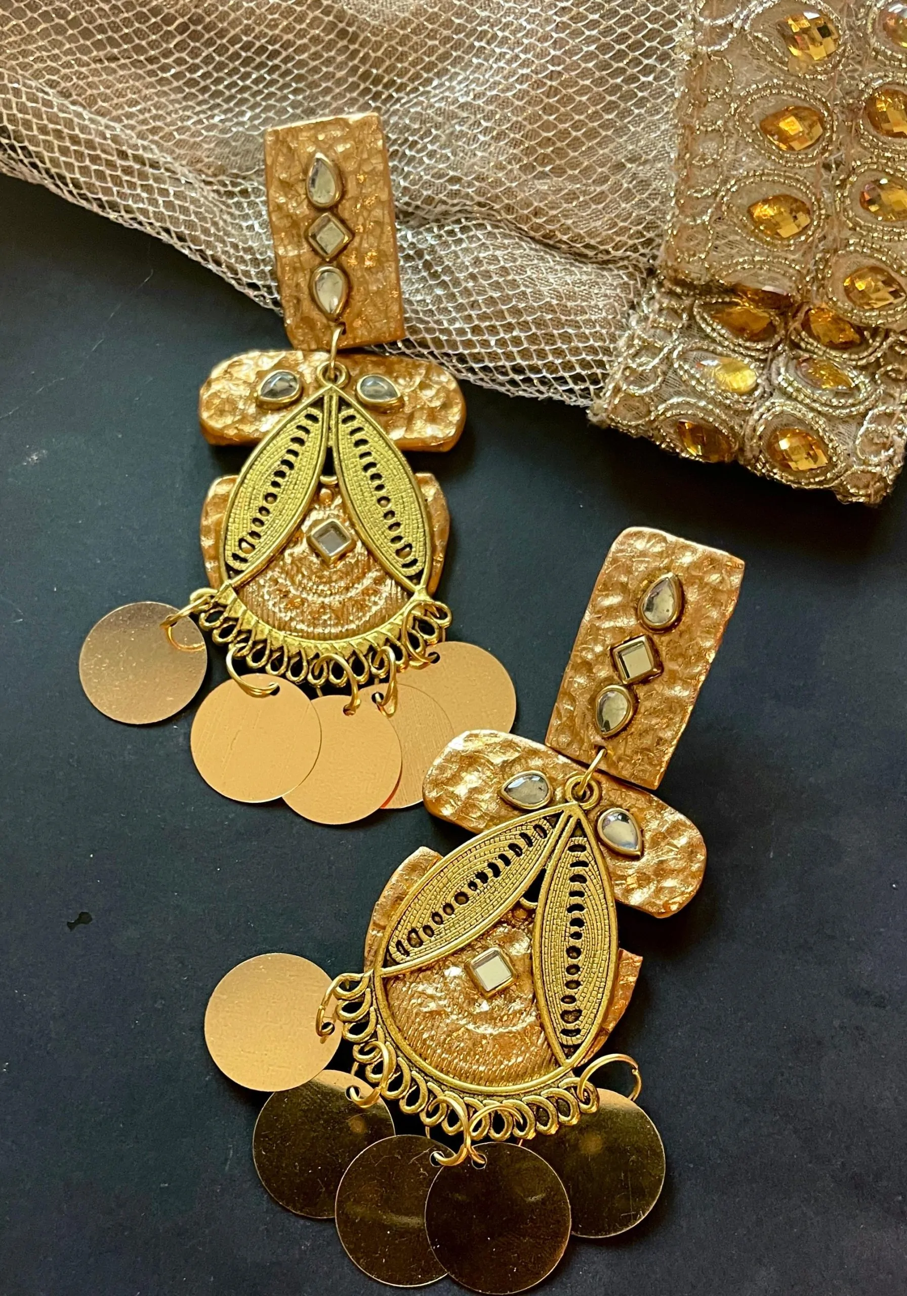 A pair of long gold dangle earrings with polymer clay, hammered metal, mirror stones, and gold coin charms, perfect for wedding and festive jewelry looks.