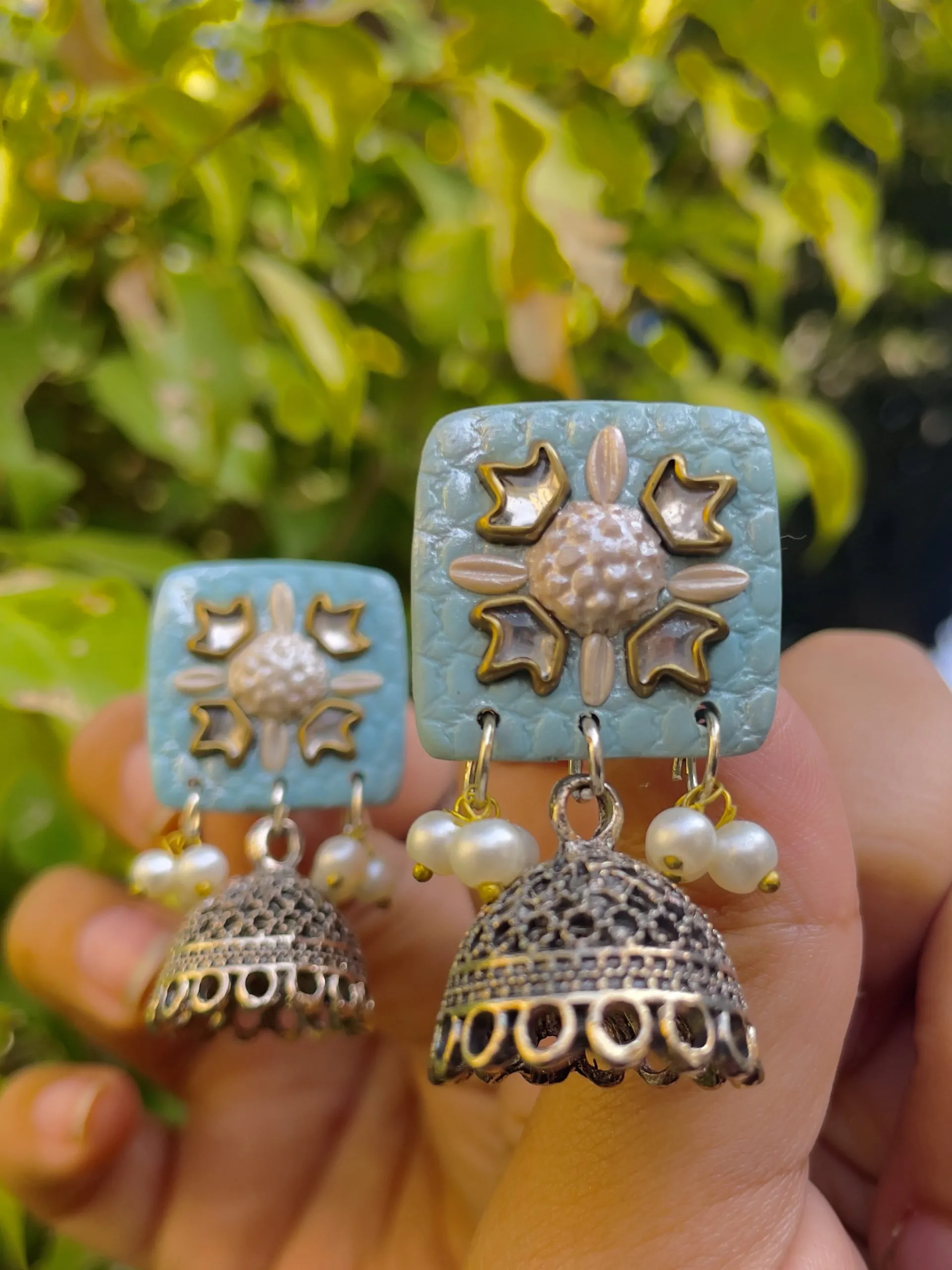 :Sky blue square textured earrings with silver floral work and Jhumka bell drops.