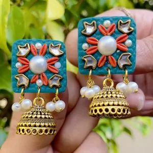 Teal square textured earrings with coral floral accents, gold Jhumka bells, and white pearls.