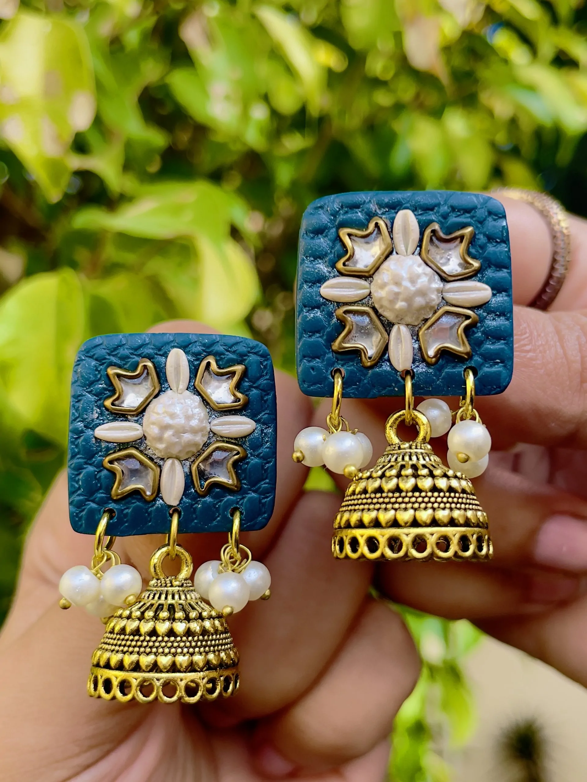 Deep teal square textured earrings with silver-toned floral work and Jhumka bell drops.