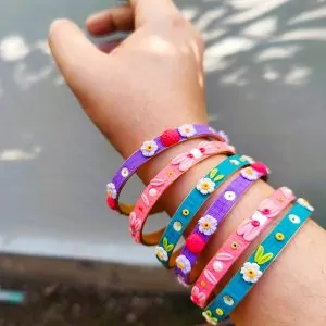 A stack of colorful artisan bangles featuring 3D clay flowers, gold thread work, and shimmering sequin accents.