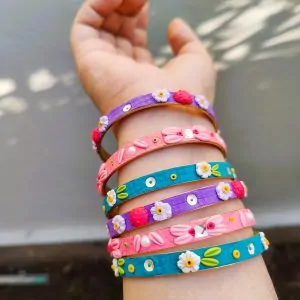 A stack of colorful artisan bangles featuring 3D clay flowers, gold thread work, and shimmering sequin accents.