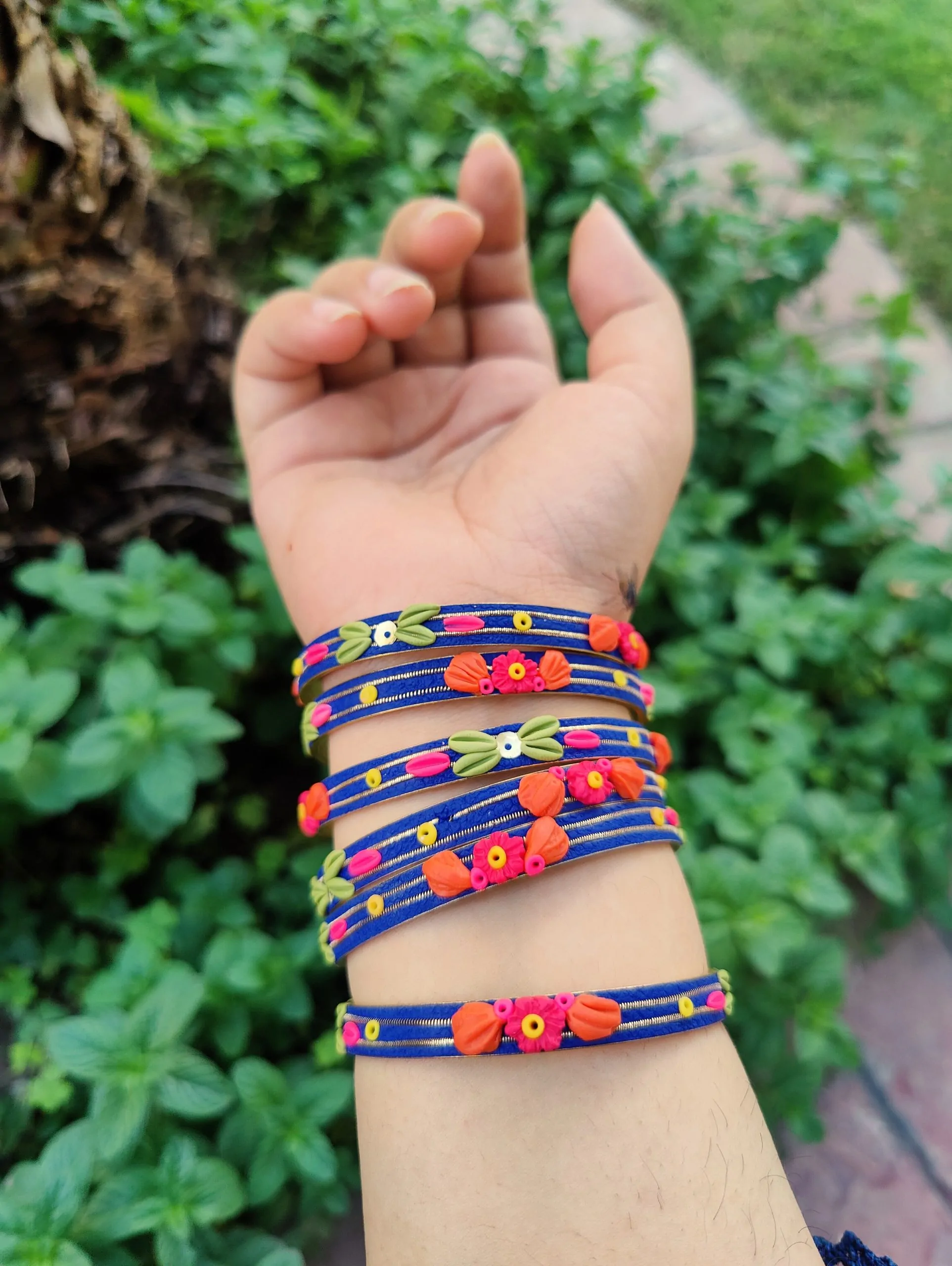 Artisan stack of royal blue textured bangles featuring hand-sculpted pink and orange clay flowers with silver metallic threading."