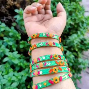 Artisan stack of emerald green textured bangles featuring hand-sculpted orange and pink clay flowers with silver sequin accents.