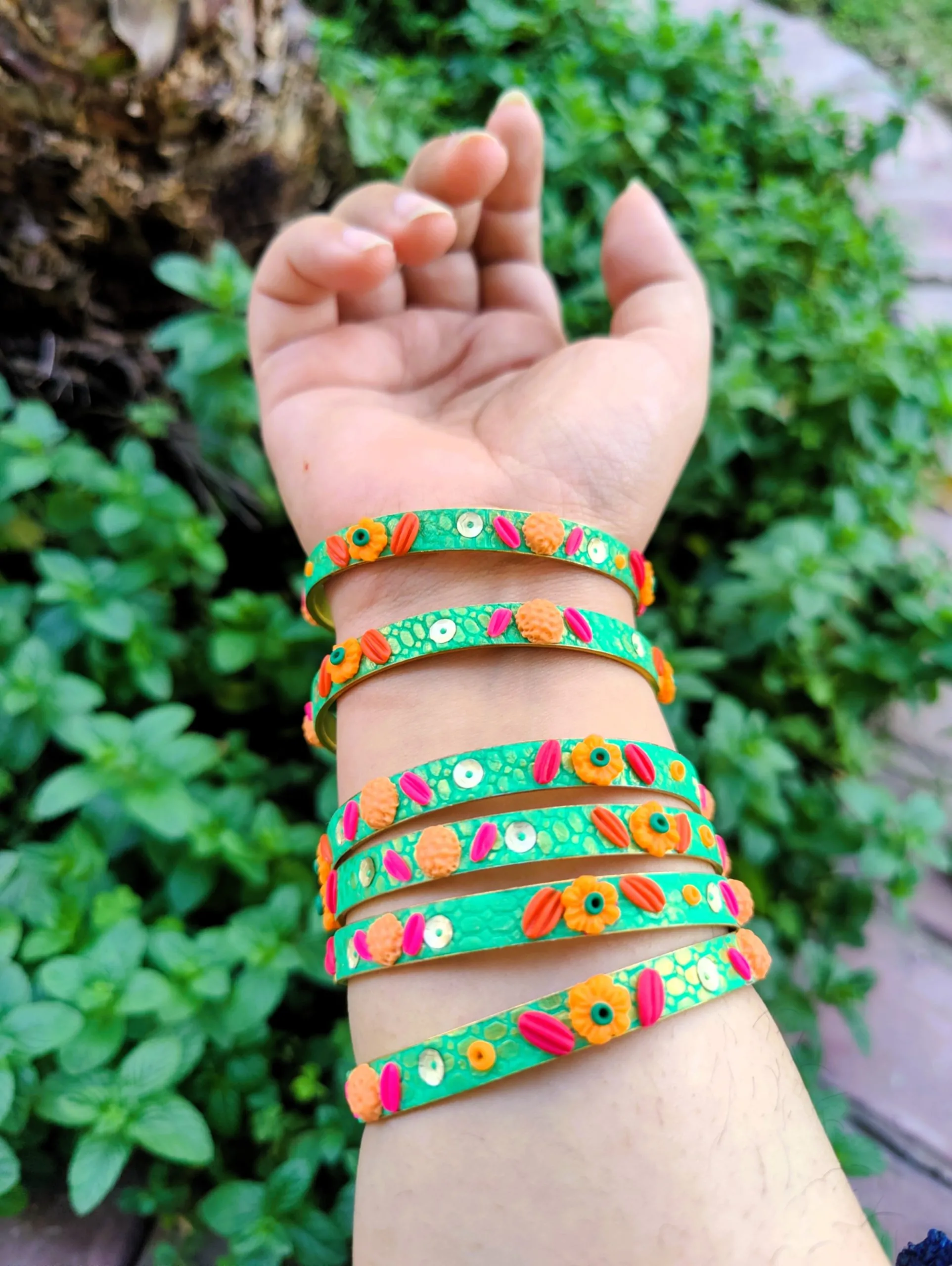 IMG20240405163745 Artisan stack of emerald green textured bangles featuring hand-sculpted orange and pink clay flowers with silver sequin accents.