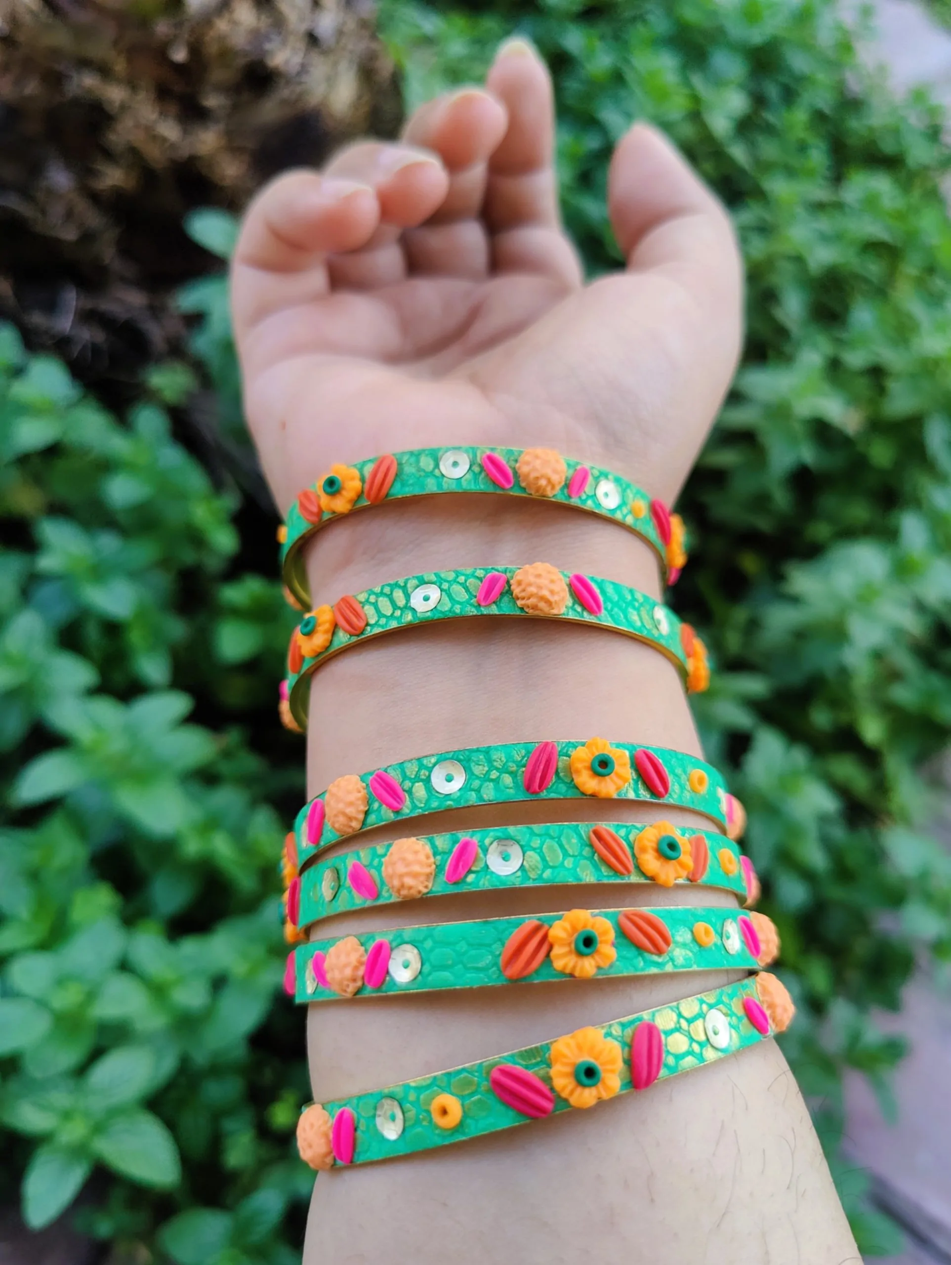 IMG20240405163748 Artisan stack of emerald green textured bangles featuring hand-sculpted orange and pink clay flowers with silver sequin accents.