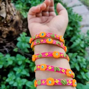 Artisan stack of magenta pink textured bangles featuring hand-sculpted orange clay flowers, green leaves, and gold metallic embroidery.