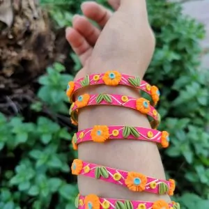 Artisan stack of magenta pink textured bangles featuring hand-sculpted orange clay flowers, green leaves, and gold metallic embroidery.