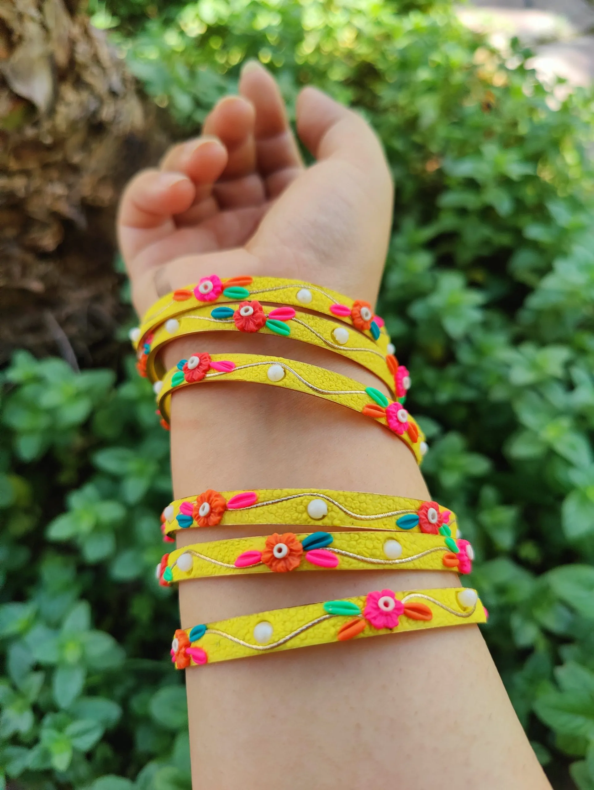 Artisan stack of funky yellow textured bangles with multicolored 3D clay flowers, gold metallic thread, and white pearl accents.