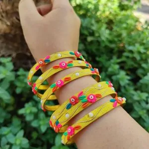 Artisan stack of funky yellow textured bangles with multicolored 3D clay flowers, gold metallic thread, and white pearl accents.