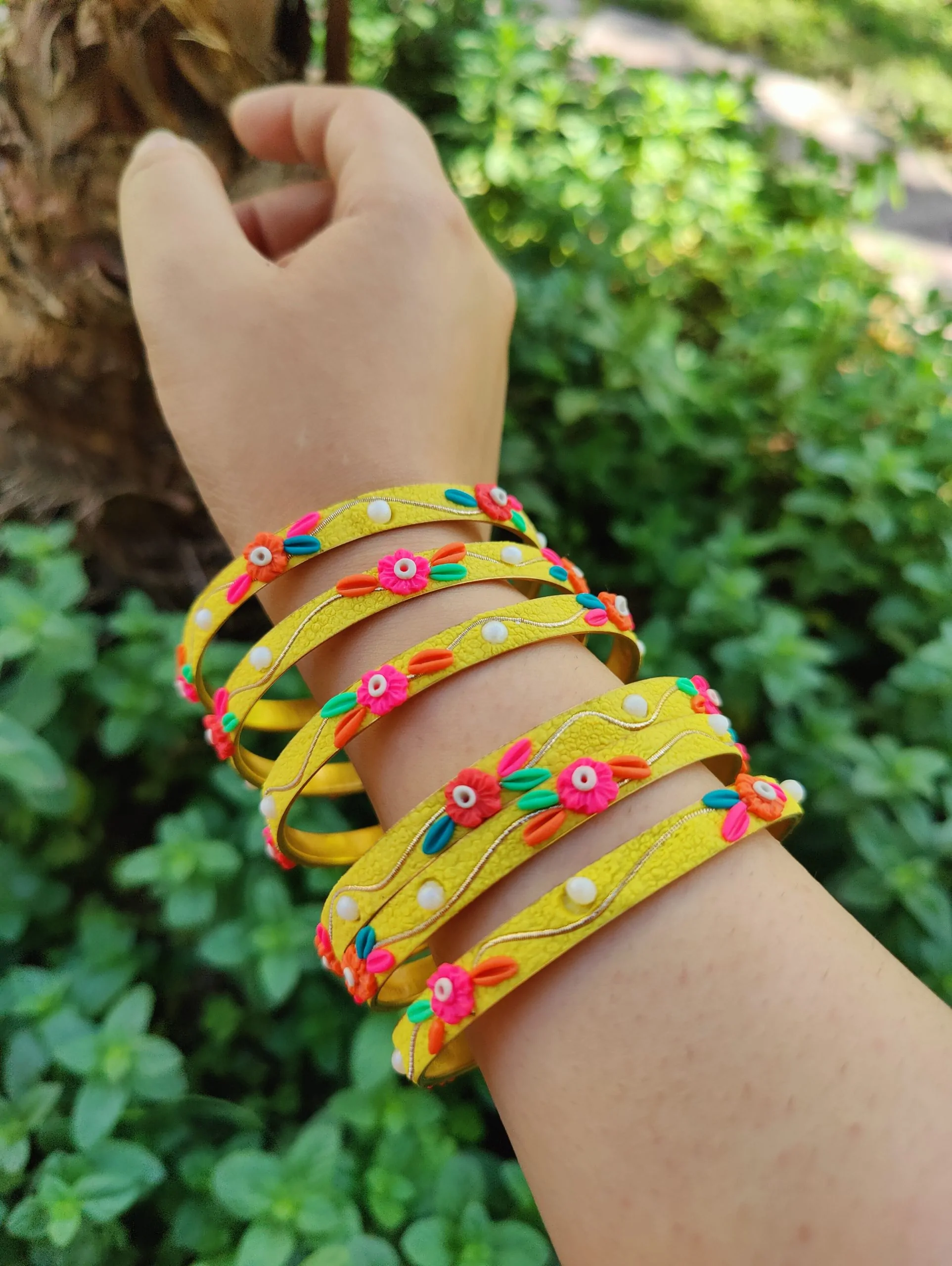 Artisan stack of funky yellow textured bangles with multicolored 3D clay flowers, gold metallic thread, and white pearl accents.