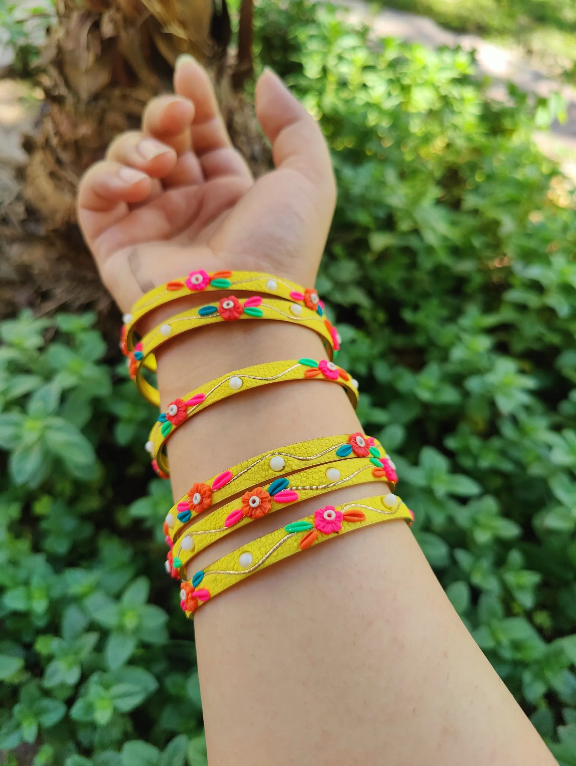 Artisan stack of funky yellow textured bangles with multicolored 3D clay flowers, gold metallic thread, and white pearl accents.