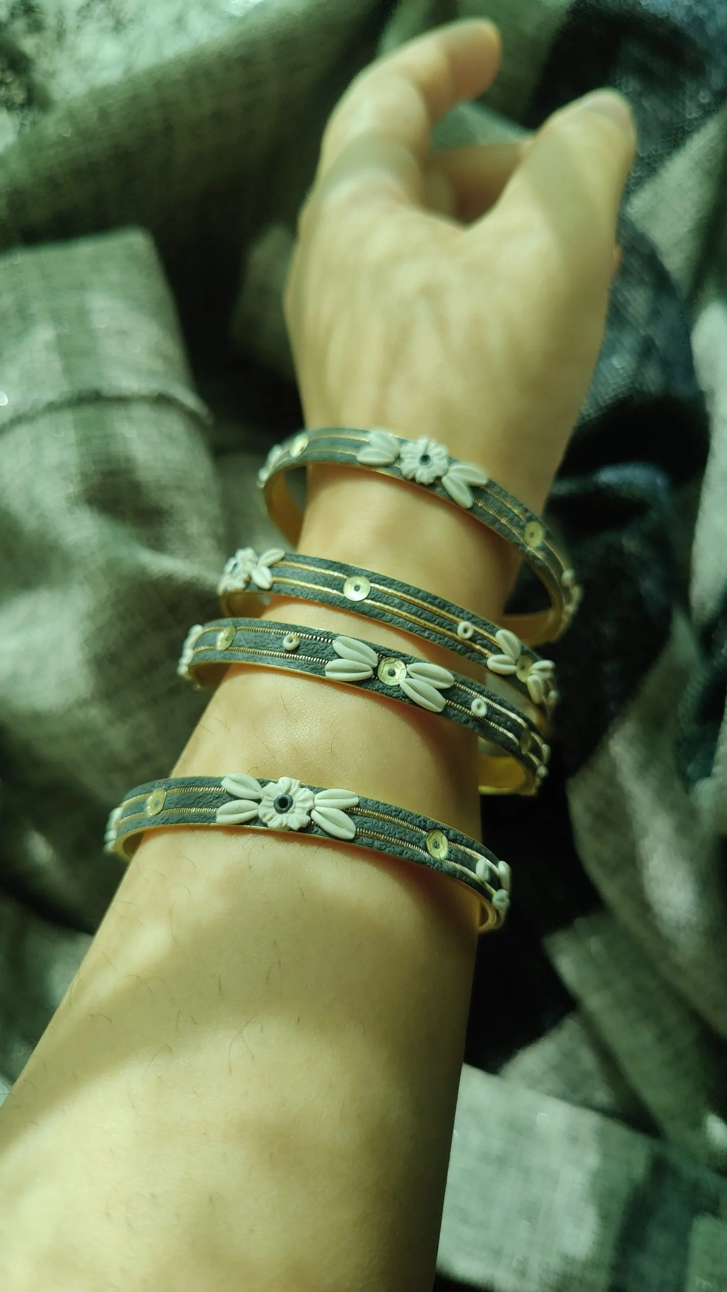 IMG20240502153512 Artisan stack of charcoal grey textured bangles featuring hand-sculpted white clay flowers, silver sequins, and gold metallic threading."