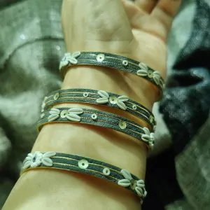 Artisan stack of charcoal grey textured bangles featuring hand-sculpted white clay flowers, silver sequins, and gold metallic threading.