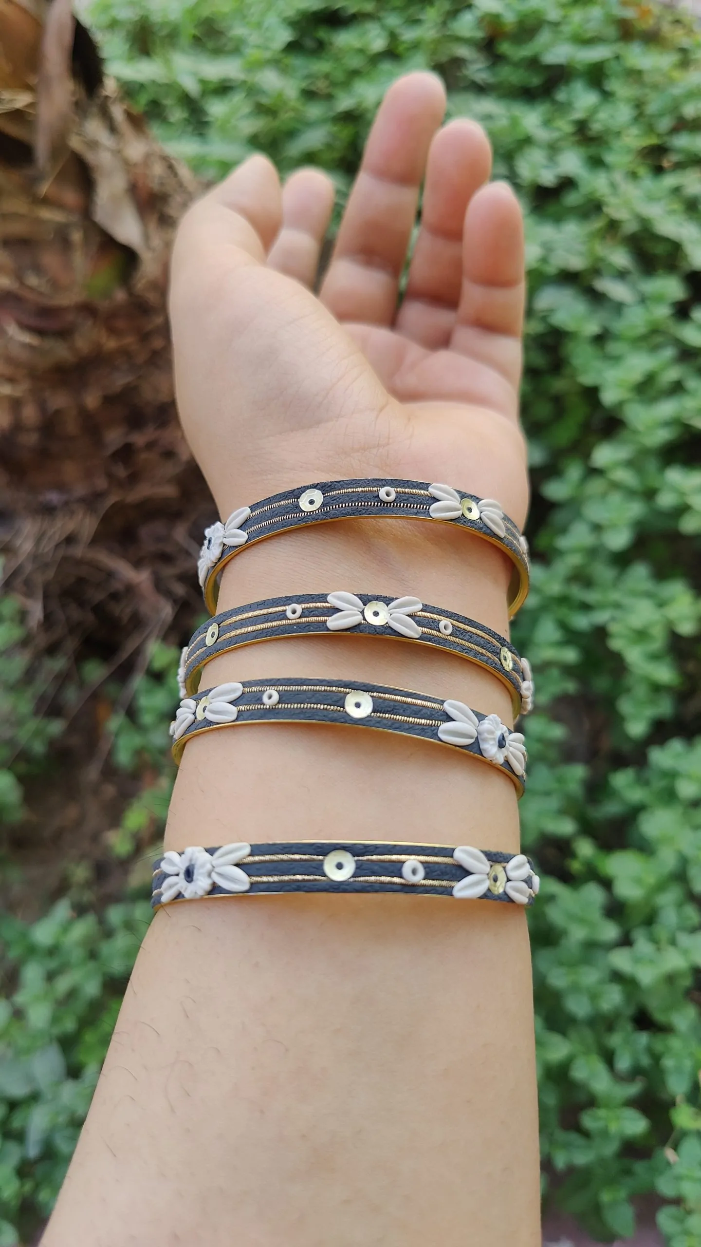 oplus_34 Artisan stack of charcoal grey textured bangles featuring hand-sculpted white clay flowers, silver sequins, and gold metallic threading."