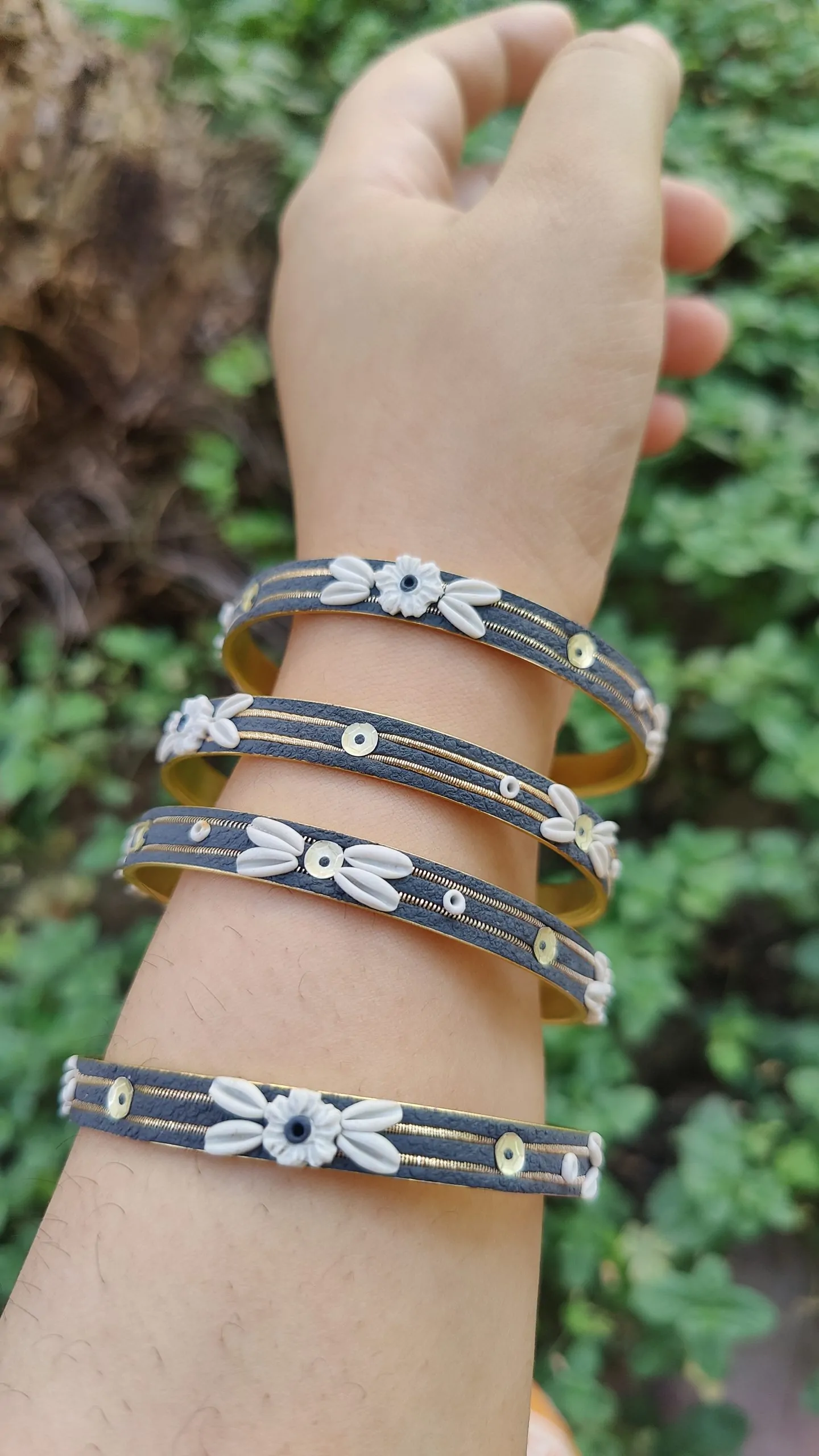 oplus_34 Artisan stack of charcoal grey textured bangles featuring hand-sculpted white clay flowers, silver sequins, and gold metallic threading.