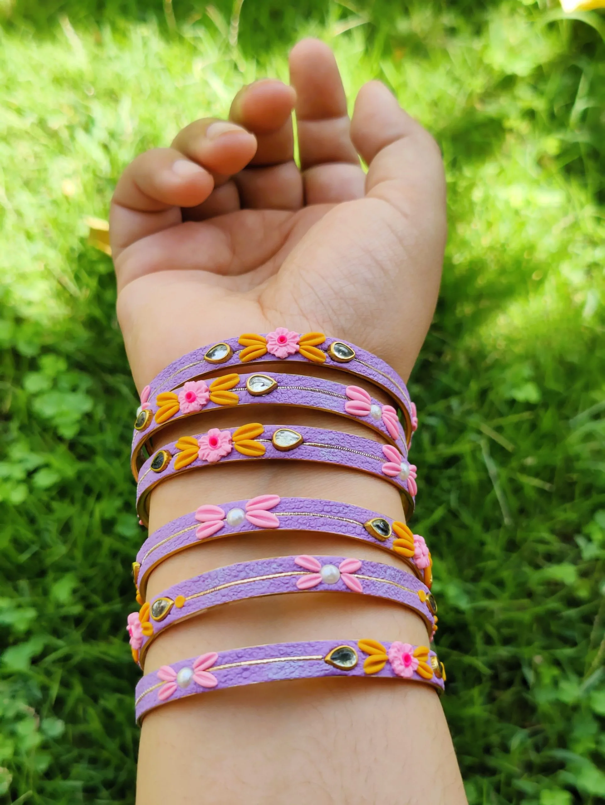 IMG20240528131743 Artisan jewelry set featuring lavender textured bangles and matching Jhumka earrings with hand-sculpted pink and yellow clay flowers, pearls, and crystals