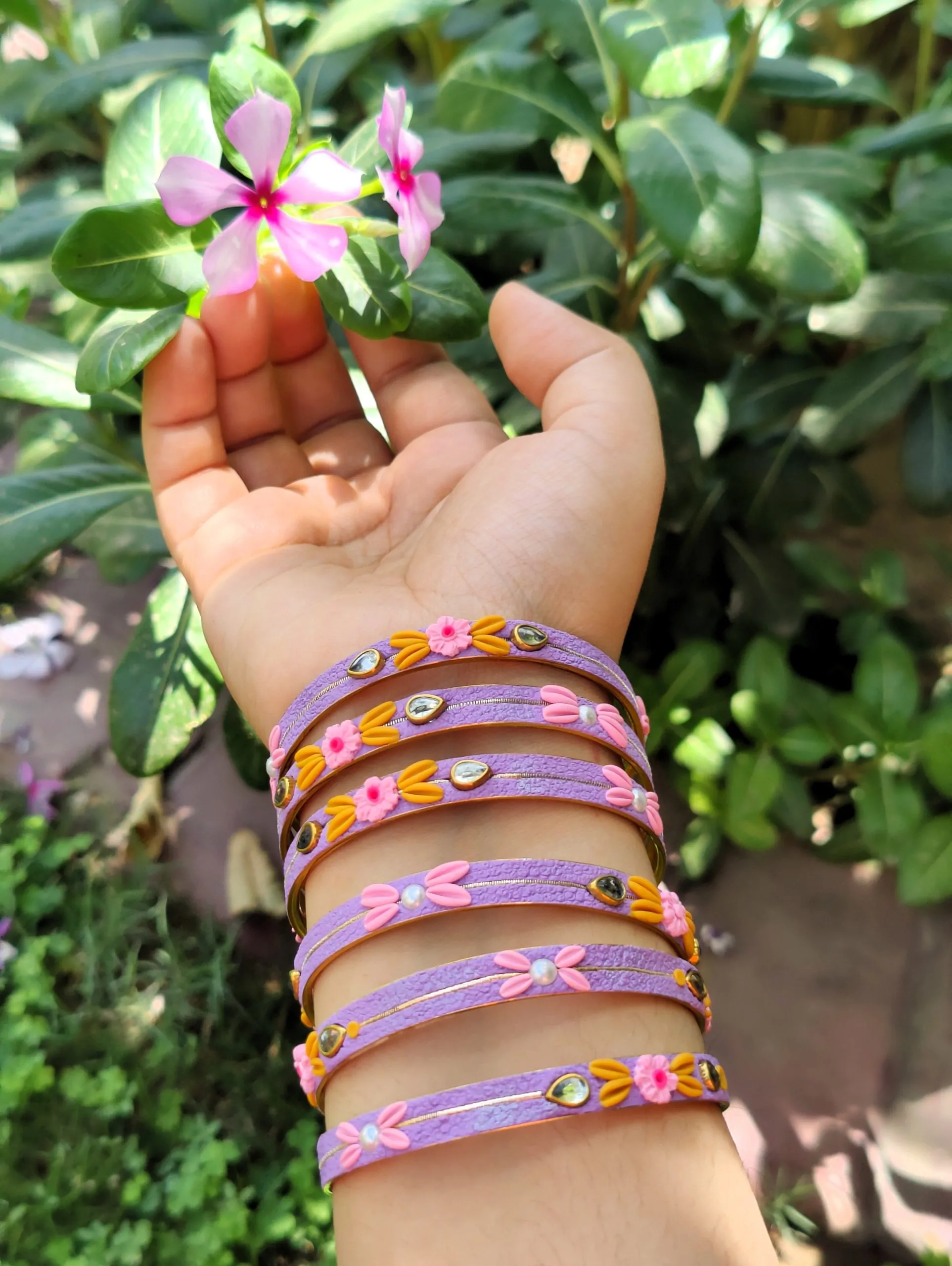 IMG20240528131813 Artisan jewelry set featuring lavender textured bangles and matching Jhumka earrings with hand-sculpted pink and yellow clay flowers, pearls, and crystals