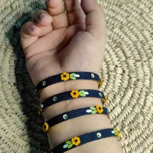 Artisan stack of black textured bangles featuring hand-sculpted 3D yellow clay flowers and silver sequin accents.
