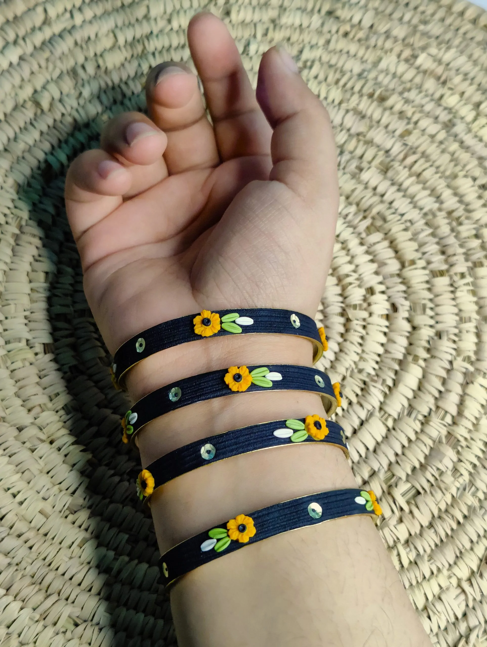 Artisan stack of black textured bangles featuring hand-sculpted 3D yellow clay flowers and silver sequin accents."