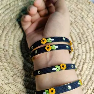Artisan stack of black textured bangles featuring hand-sculpted 3D yellow clay flowers and silver sequin accents.