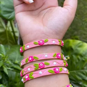 Artisan stack of candy pink textured bangles featuring hand-sculpted pink clay flowers, green leaves, white pearls, and gold metallic threading
