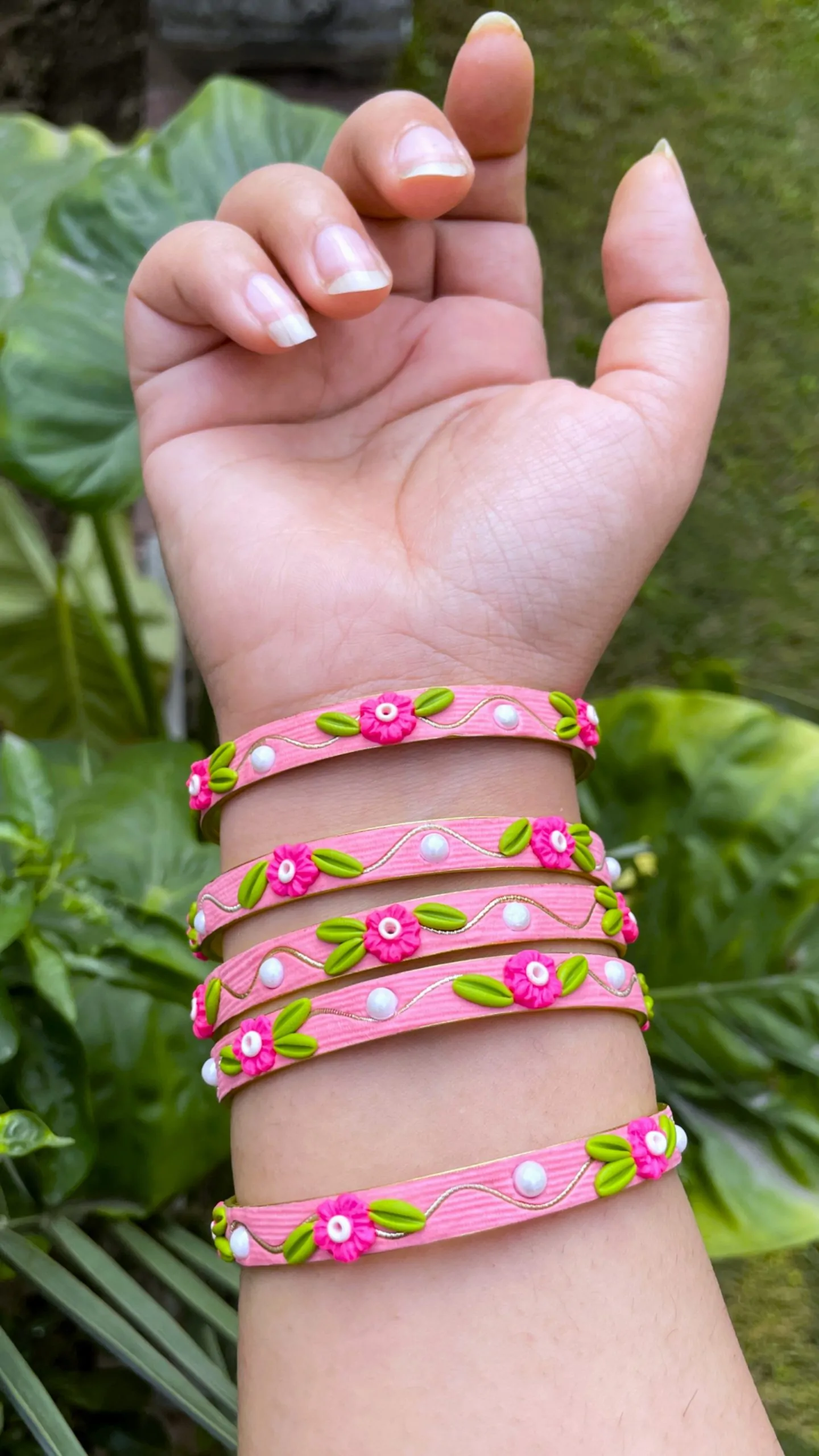 Artisan stack of candy pink textured bangles featuring hand-sculpted pink clay flowers, green leaves, white pearls, and gold metallic threading
