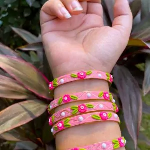 Artisan stack of candy pink textured bangles featuring hand-sculpted pink clay flowers, green leaves, white pearls, and gold metallic threading