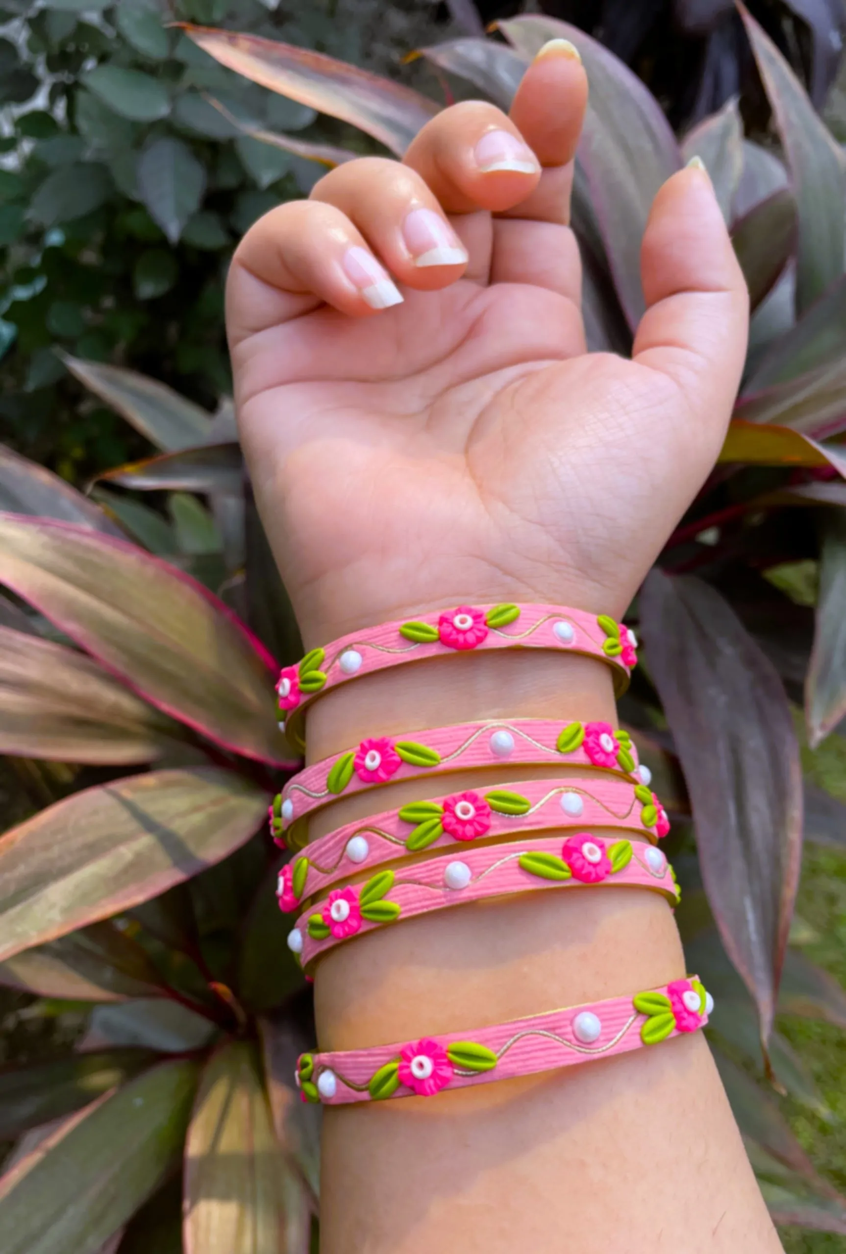 Artisan stack of candy pink textured bangles featuring hand-sculpted pink clay flowers, green leaves, white pearls, and gold metallic threading