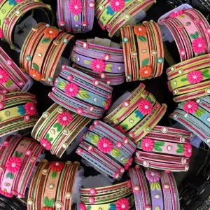 Artisan stack of lemon yellow textured bangles featuring a large 3D fuchsia clay flower, rainbow metallic embroidery, and crystal accents.