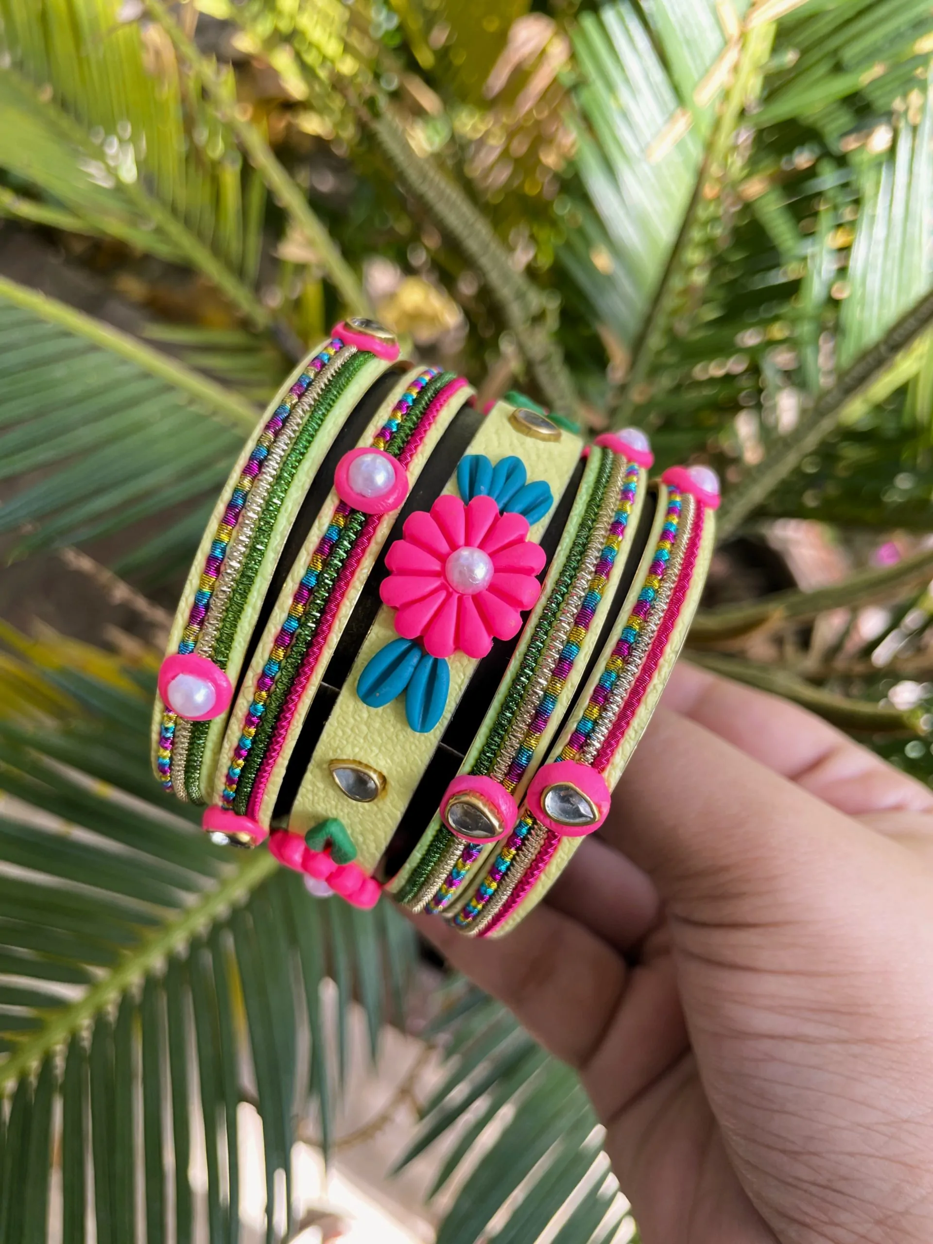 IMG_5059 Artisan stack of lemon yellow textured bangles featuring a large 3D fuchsia clay flower, rainbow metallic embroidery, and crystal accents.
