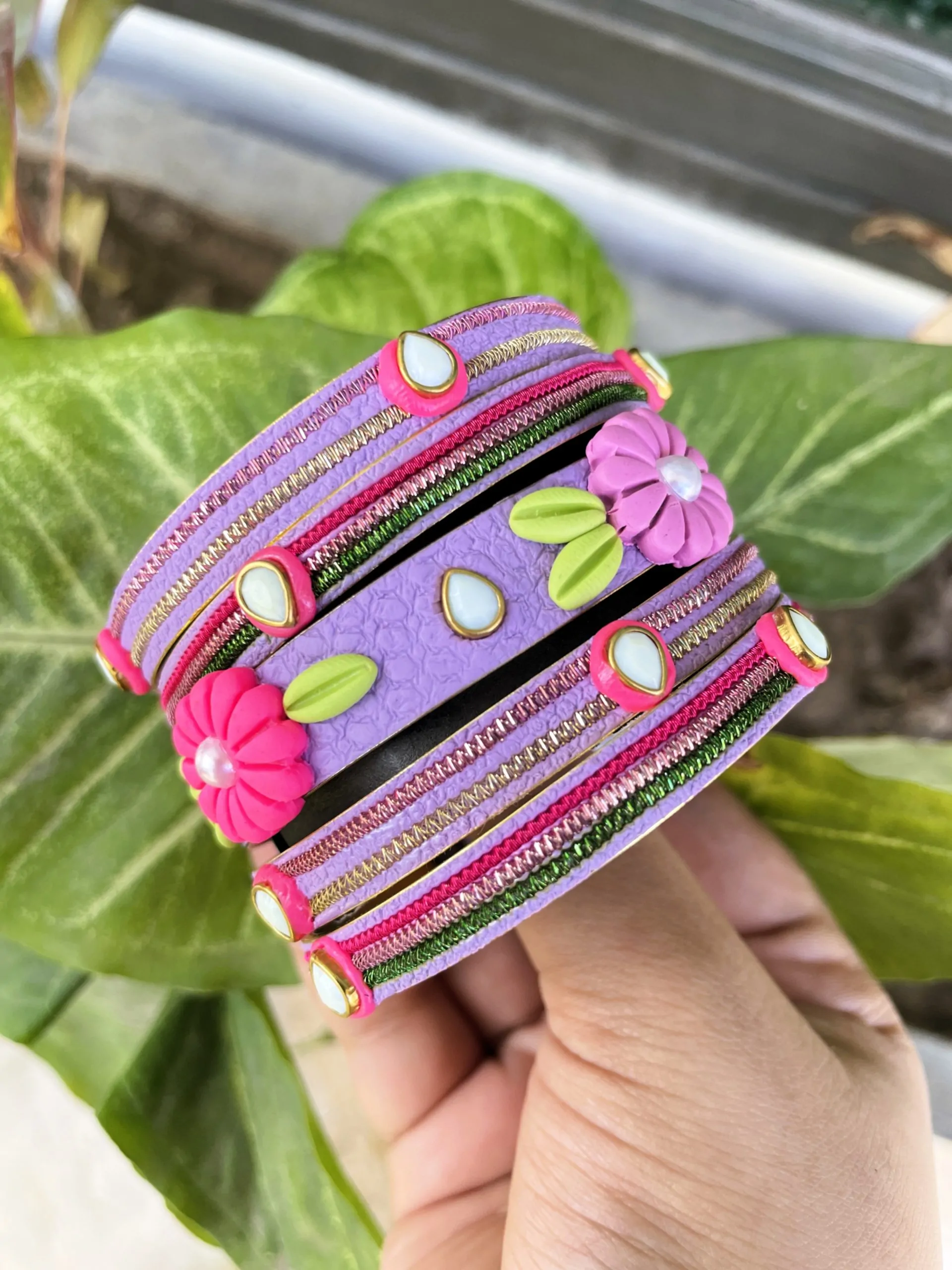 IMG_5077 rtisan stack of pastel lavender textured bangles featuring 3D clay flowers, kundan stone accents, and gold metallic embroidery.