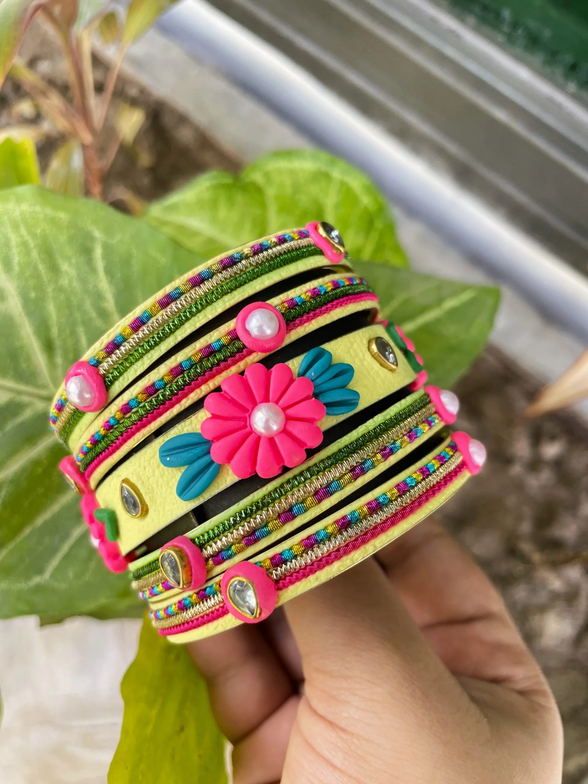 IMG_5079 Artisan stack of lemon yellow textured bangles featuring a large 3D fuchsia clay flower, rainbow metallic embroidery, and crystal accents.