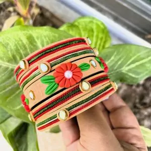 Artisan stack of peach textured bangles featuring a hand-sculpted red clay flower, kundan stone accents, and green metallic embroidery