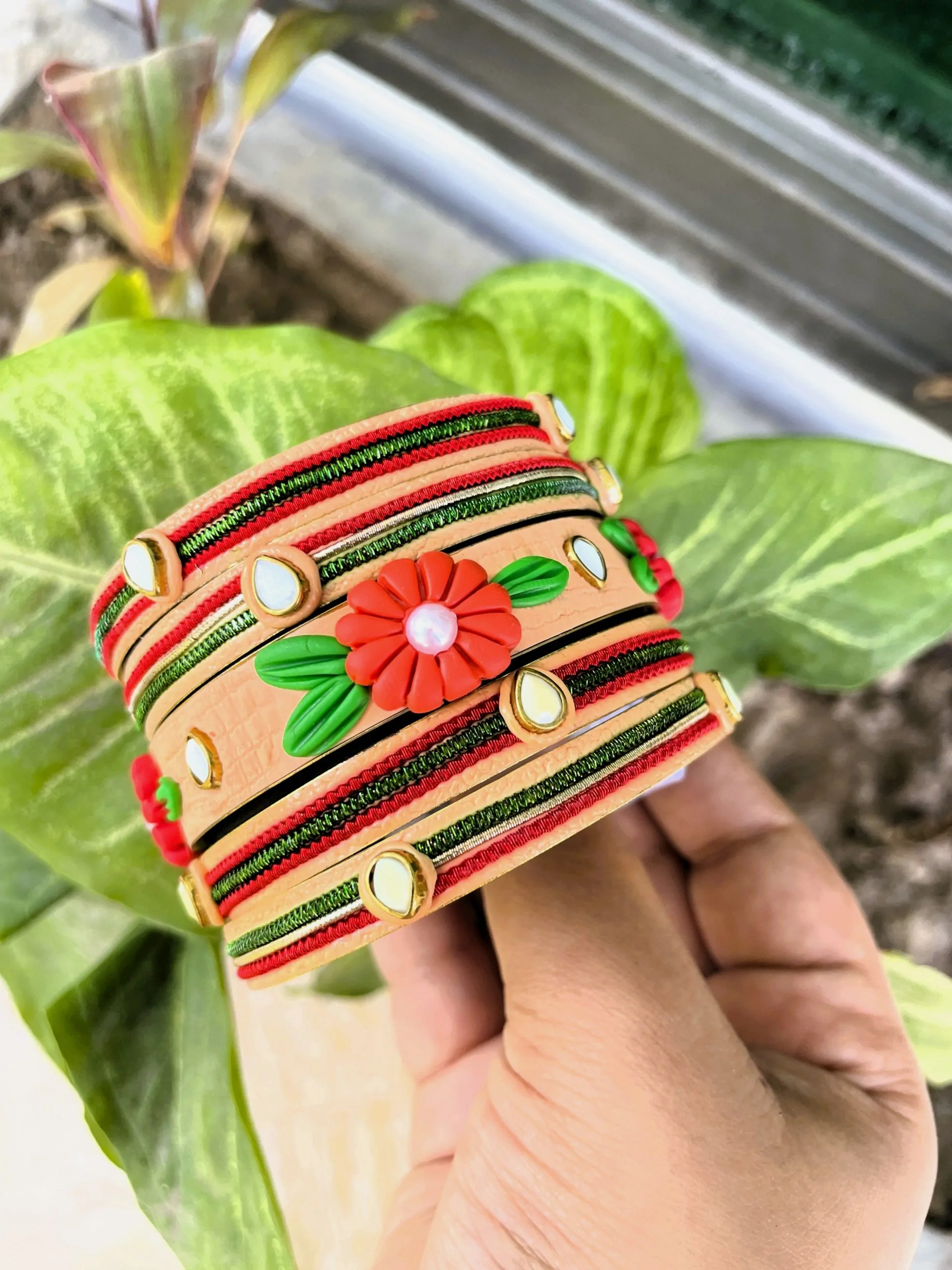 Artisan stack of peach textured bangles featuring a hand-sculpted red clay flower, kundan stone accents, and green metallic embroidery