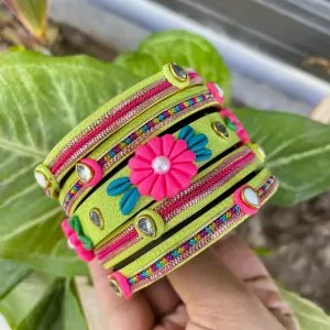 Artisan stack of neon lime green textured bangles featuring a large 3D fuchsia clay flower, rainbow metallic embroidery, and crystal accents.