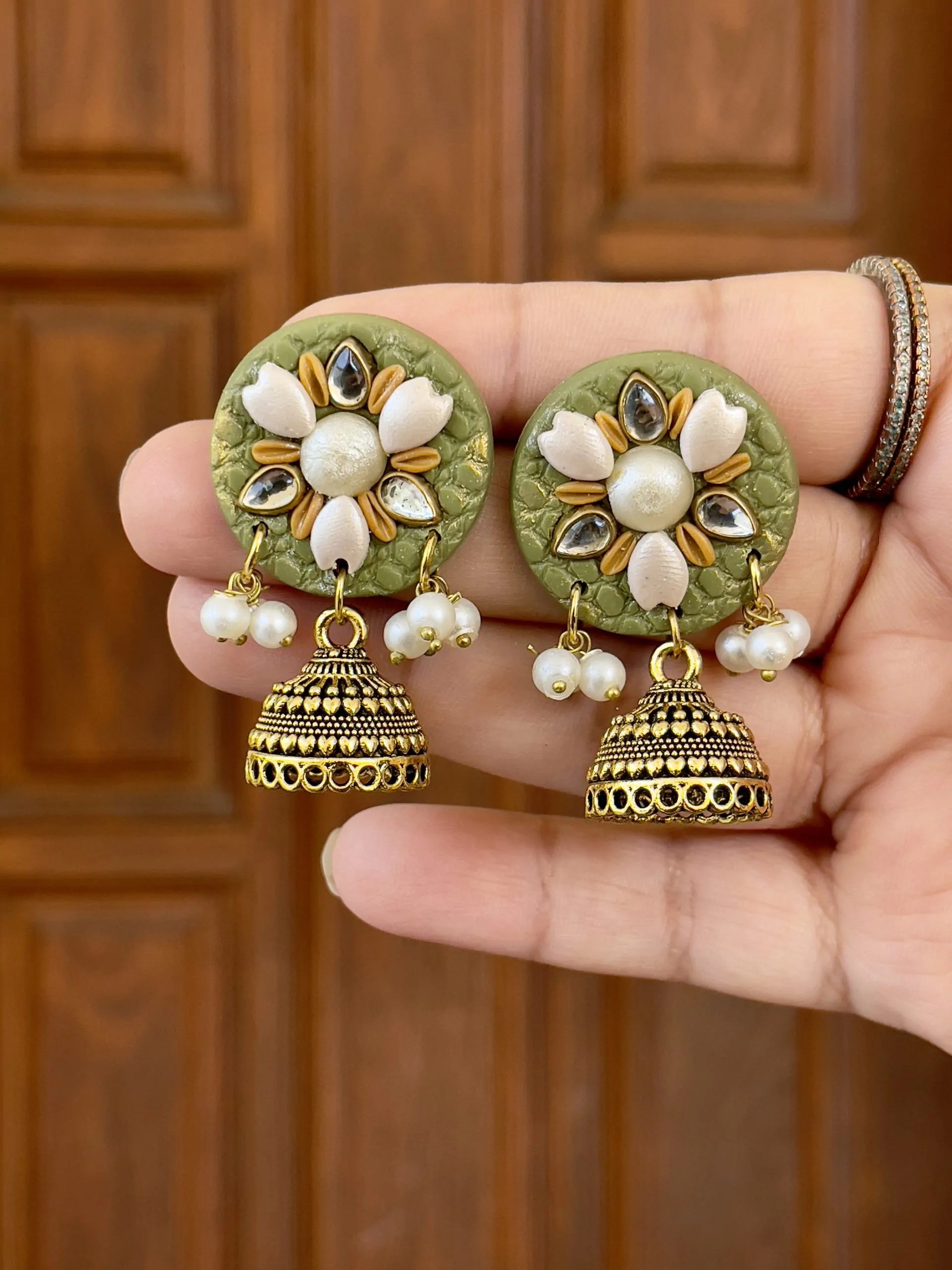 Olive green circular textured earrings with gold floral work and Jhumka bells.