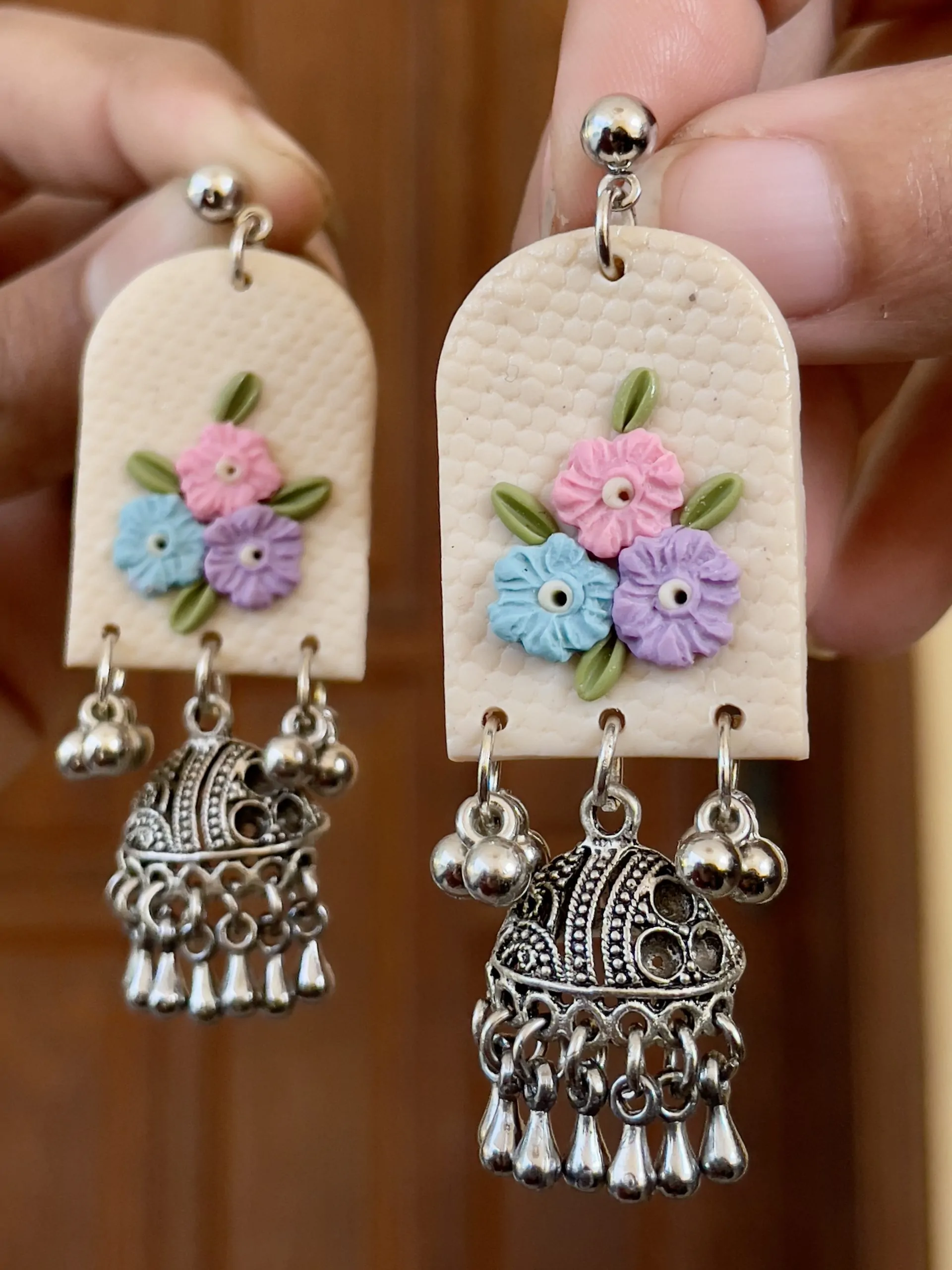 Arched cream earrings with sky blue, pink, and lavender flowers and silver Ghungroo Jhumkas