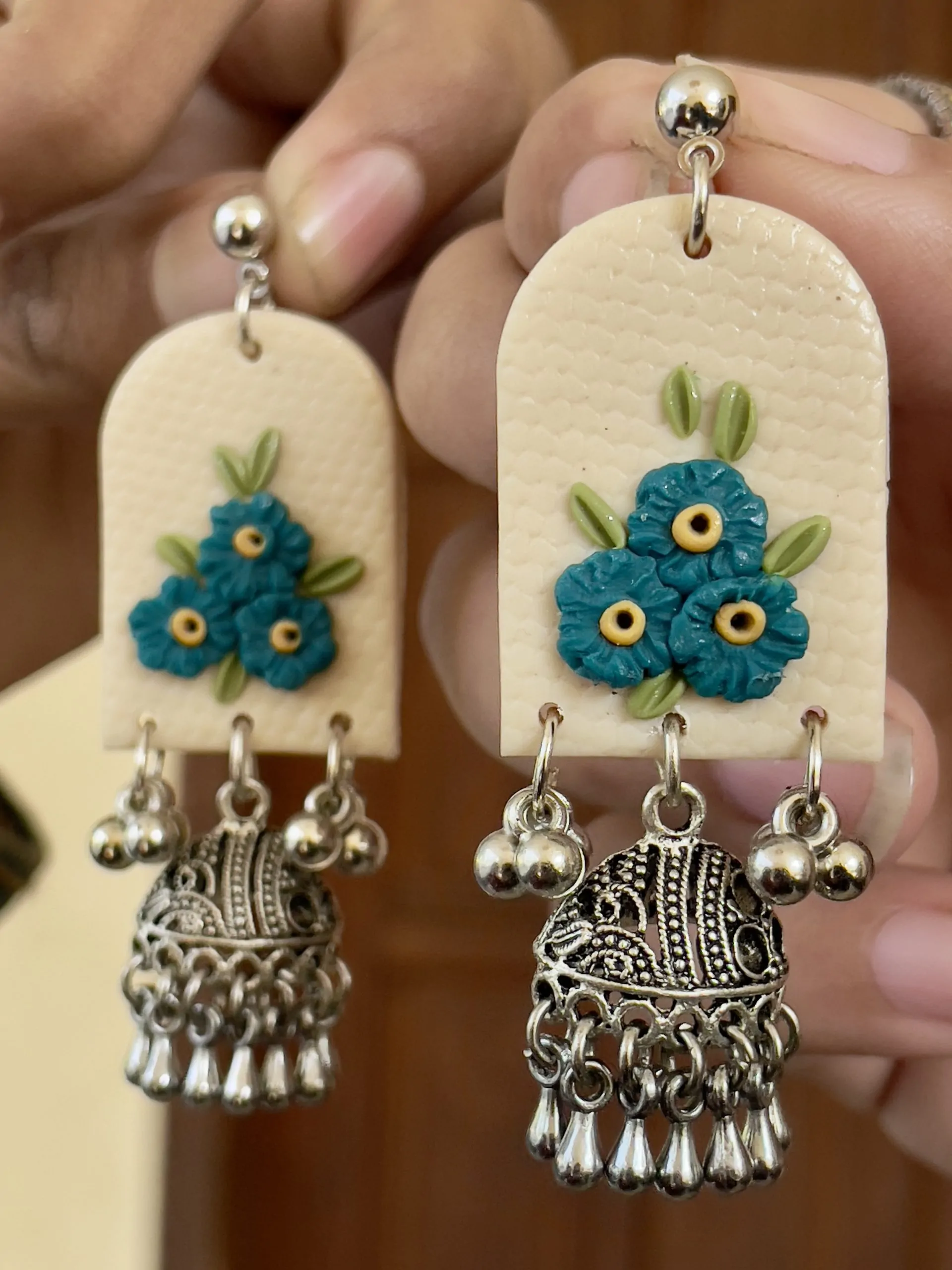 Arched textured earrings with teal blue floral cluster and heavy silver Ghungroo bell drops.