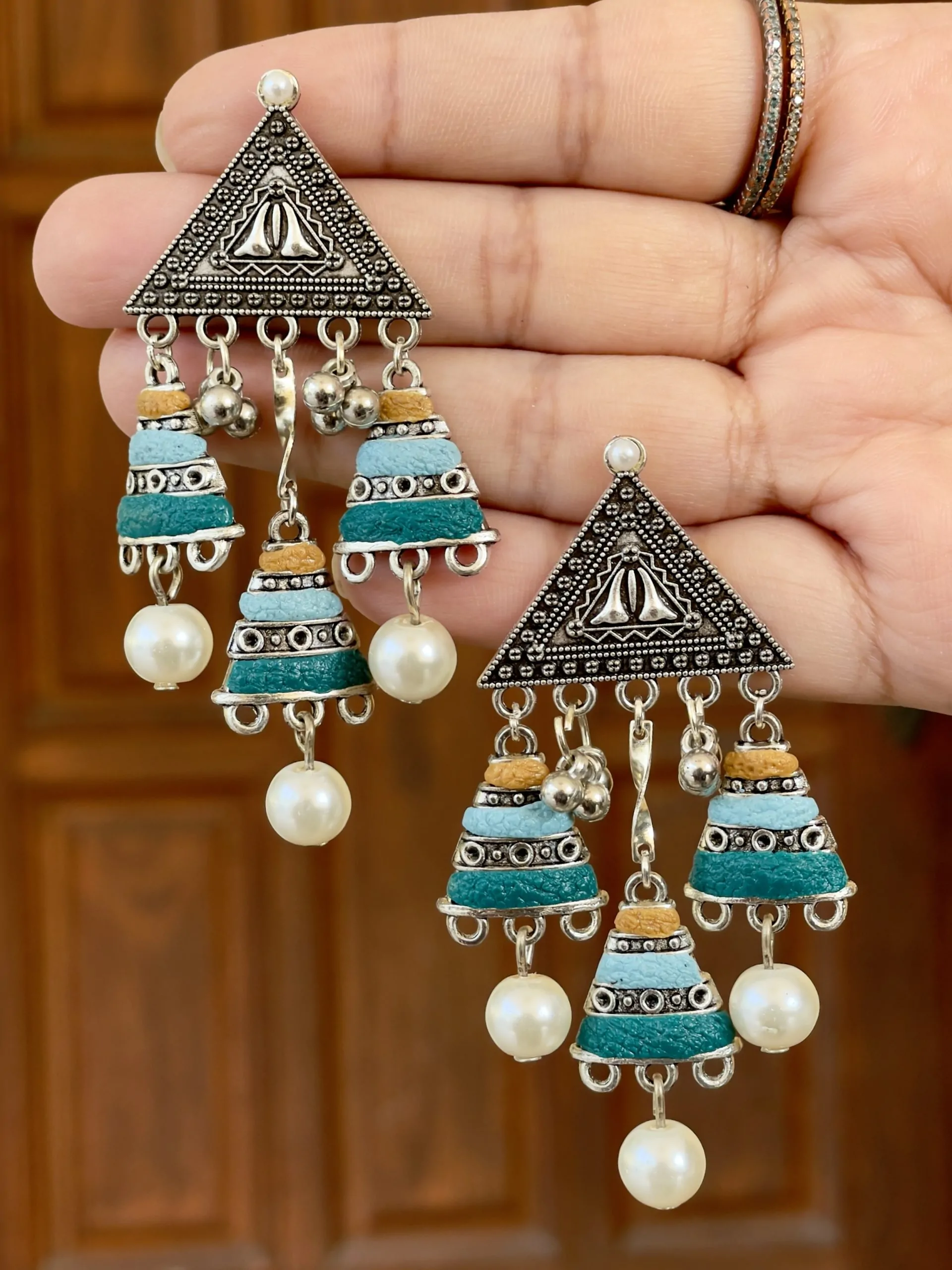 Antiqued silver triangular statement earrings with three tiers of mustard yellow, sky blue, and teal blue beads and small silver bell charms.