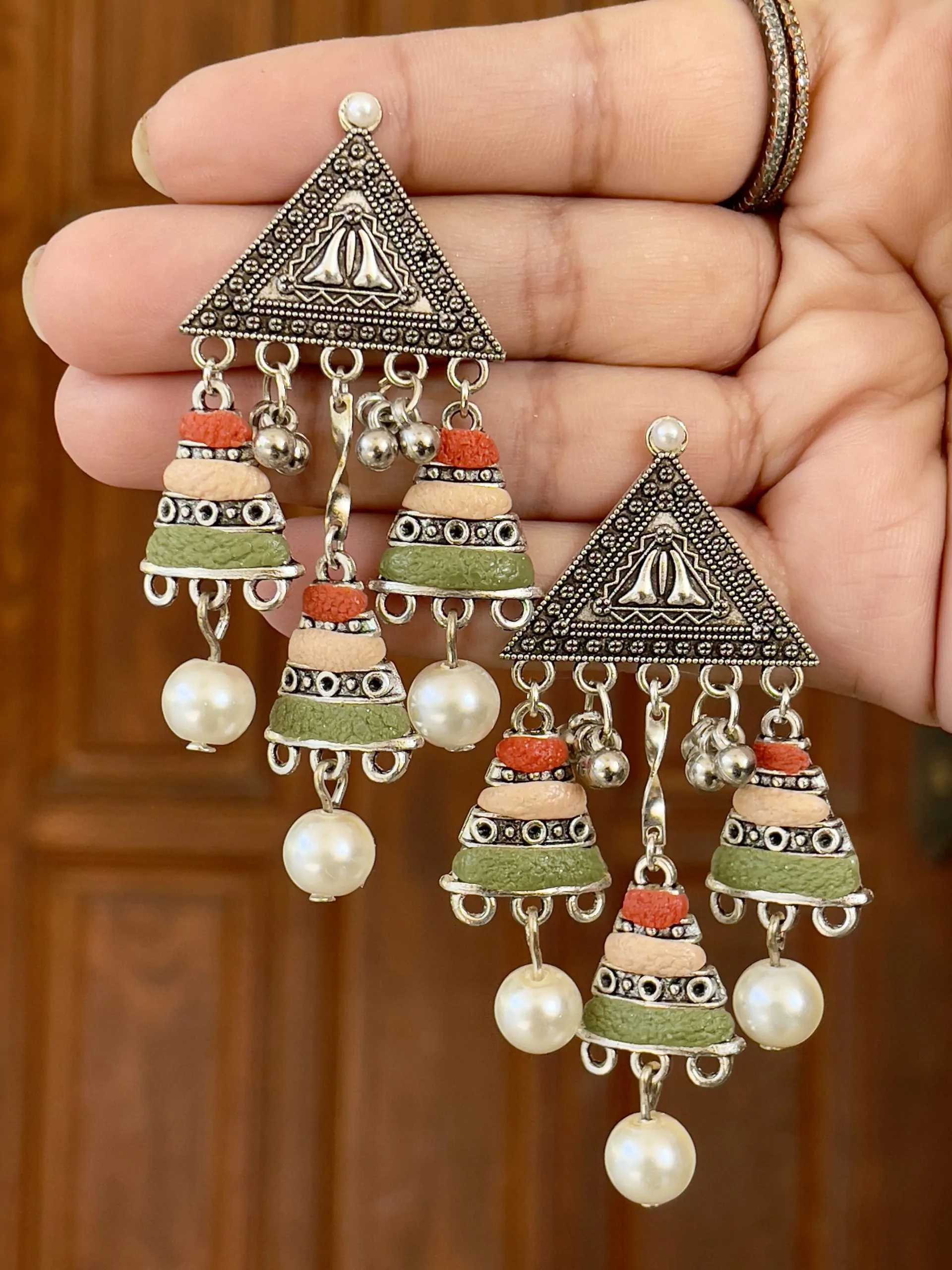 Handcrafted oxidized silver triangular earrings featuring a triple-tier tassel of terracotta red, peach, and olive green textured beads with pearl drops.