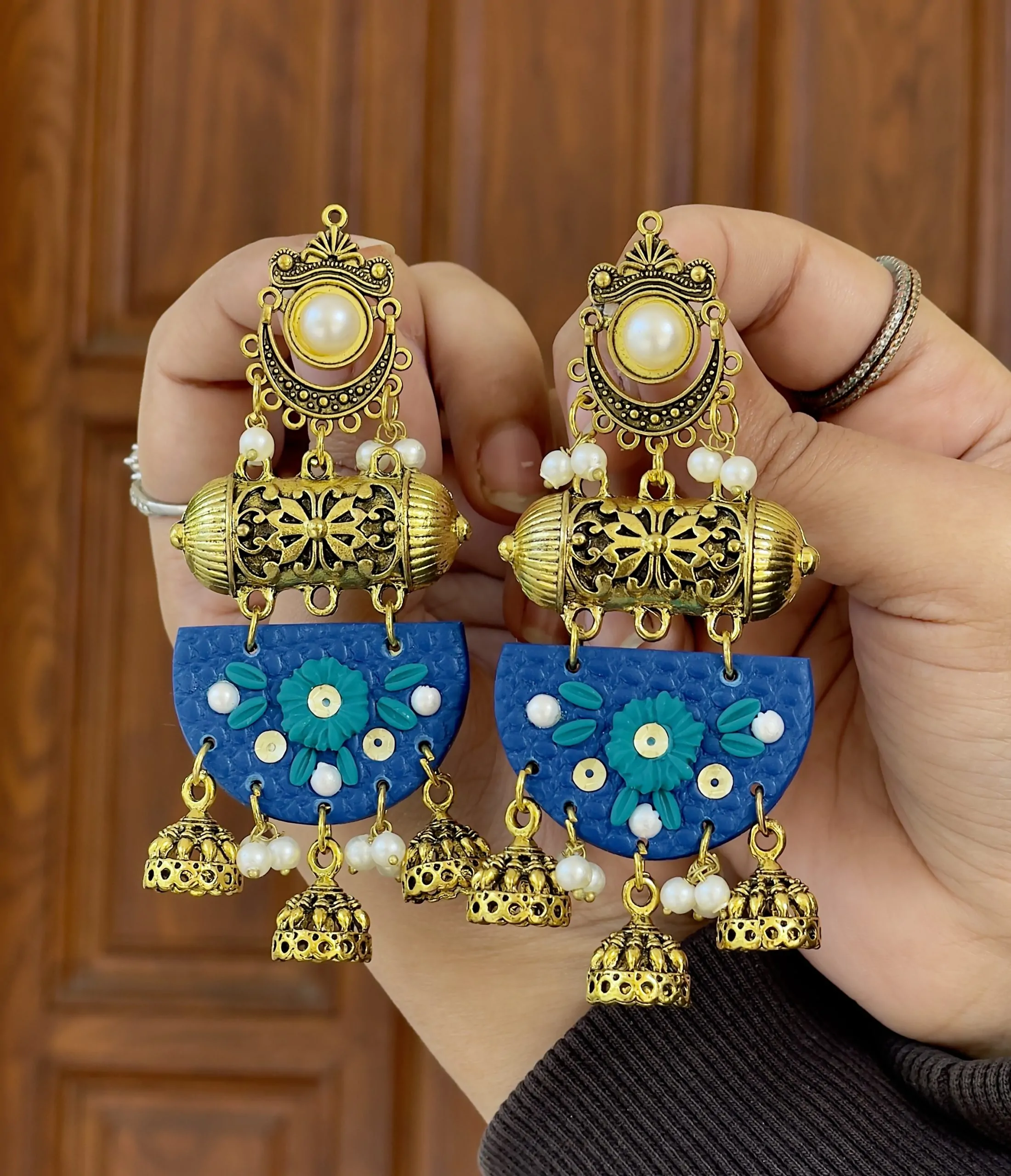 Close-up of textured blue half-moon earrings with teal flowers and gold-toned traditional dangles.
